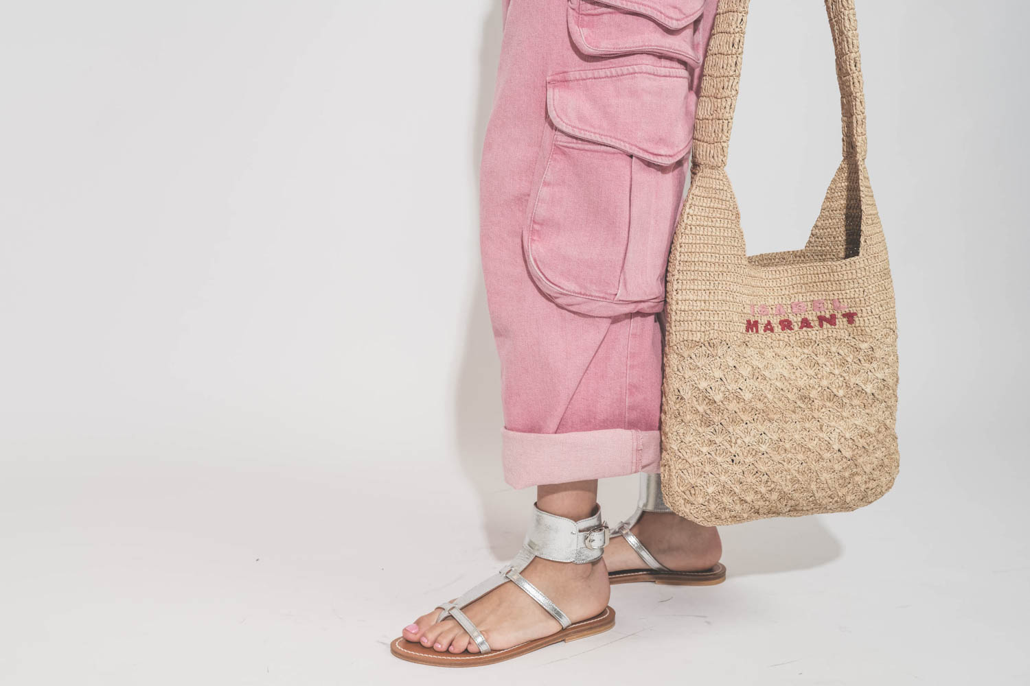 Sac en raphia naturel logo Isabel Marant brodé rose et rouge Praia Isabel Marant. Porté main avec un jean multi-poches rose Cargo rose R13 et des sandales en cuir argent Caravelle K.Jacques St-Tropez. 