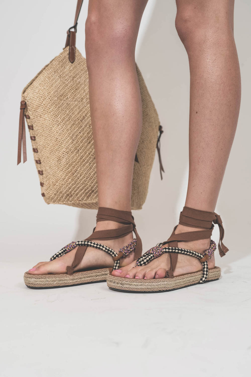 Sandales entre-doigts en cordes tressées multicolores beige et ruban beige à lacer autour des chevilles Gypsa Isabel Marant. Portées de profil avec un panier en osier naturel et cognac Tampa Isabel Marant.