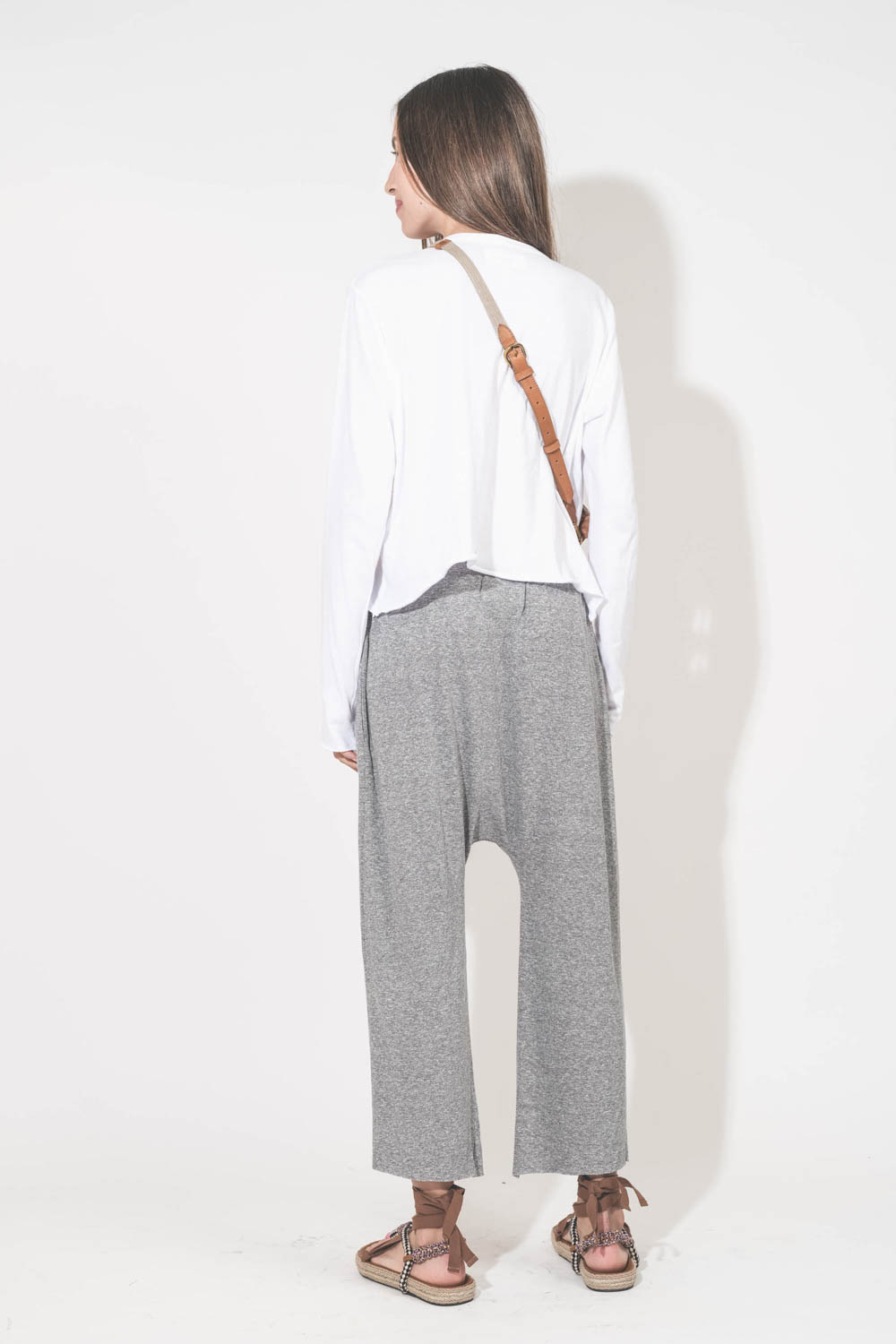 Bandoulière sangle amovible écru finition cuir chêne Jérôme Dreyfuss. Porté de dos avec une pochette en cuir suédé caramel Lucky Jérôme Dreyfuss. Tee-shirt manches longues court blanc The Great et pantalon sarouel en jersey gris chiné The Great. Sandales 