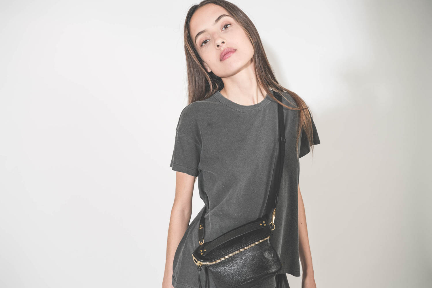 Bandoulière sangle et cuir noir finition laiton doré réglable avec une boucle esprit ceinture Jérôme Dreyfuss. Porté de face avec une pochette Lucky en cuir chèvre noir grainé Jérôme Dreyfuss. Tee-shirt manches courtes et pantalon sarouel en jersey noir d