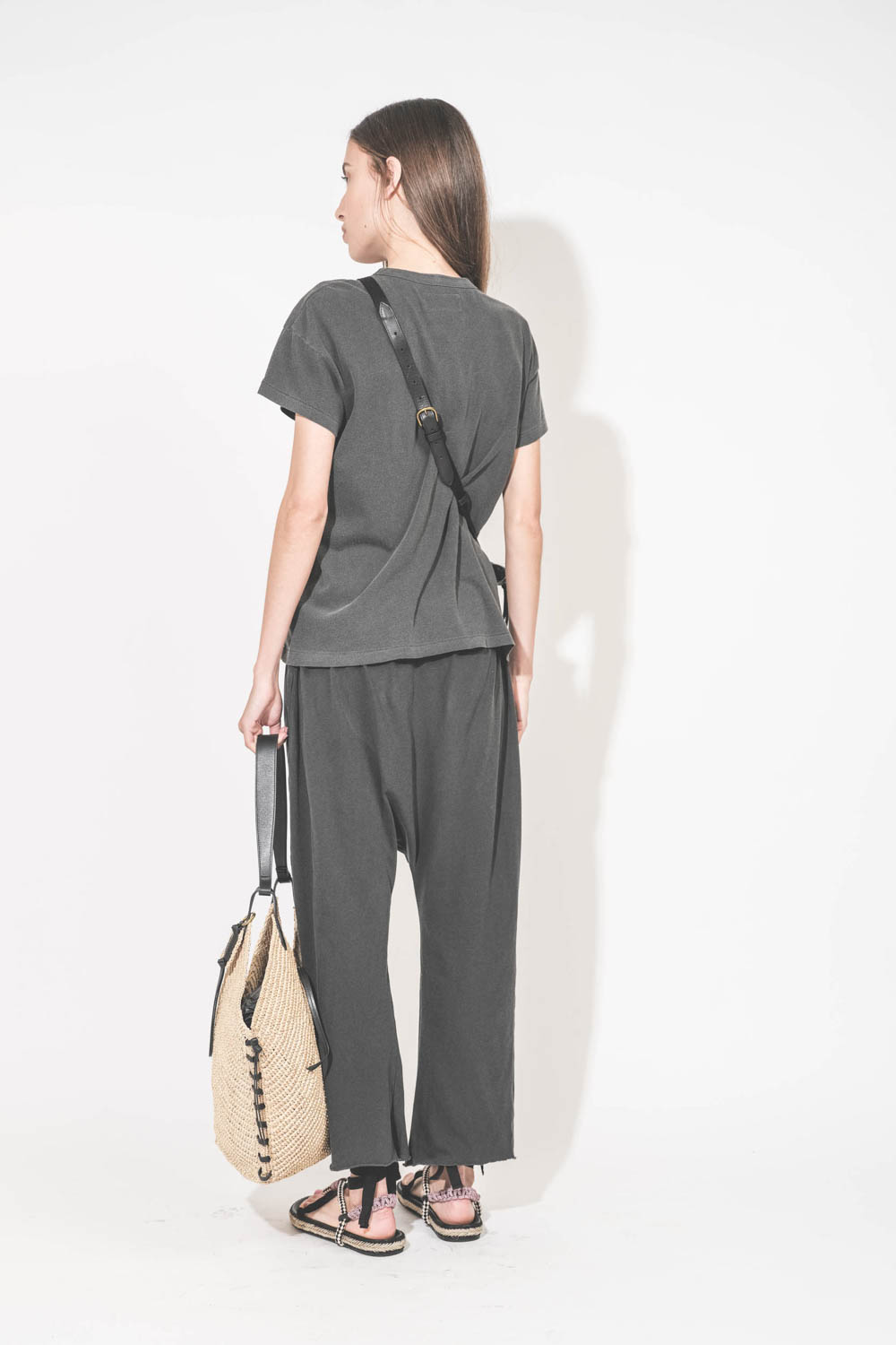Bandoulière sangle et cuir noir finition laiton doré réglable avec une boucle esprit ceinture Jérôme Dreyfuss. Porté de dos avec une pochette Lucky en cuir chèvre noir grainé Jérôme Dreyfuss. Tee-shirt manches courtes et pantalon sarouel en jersey noir dé