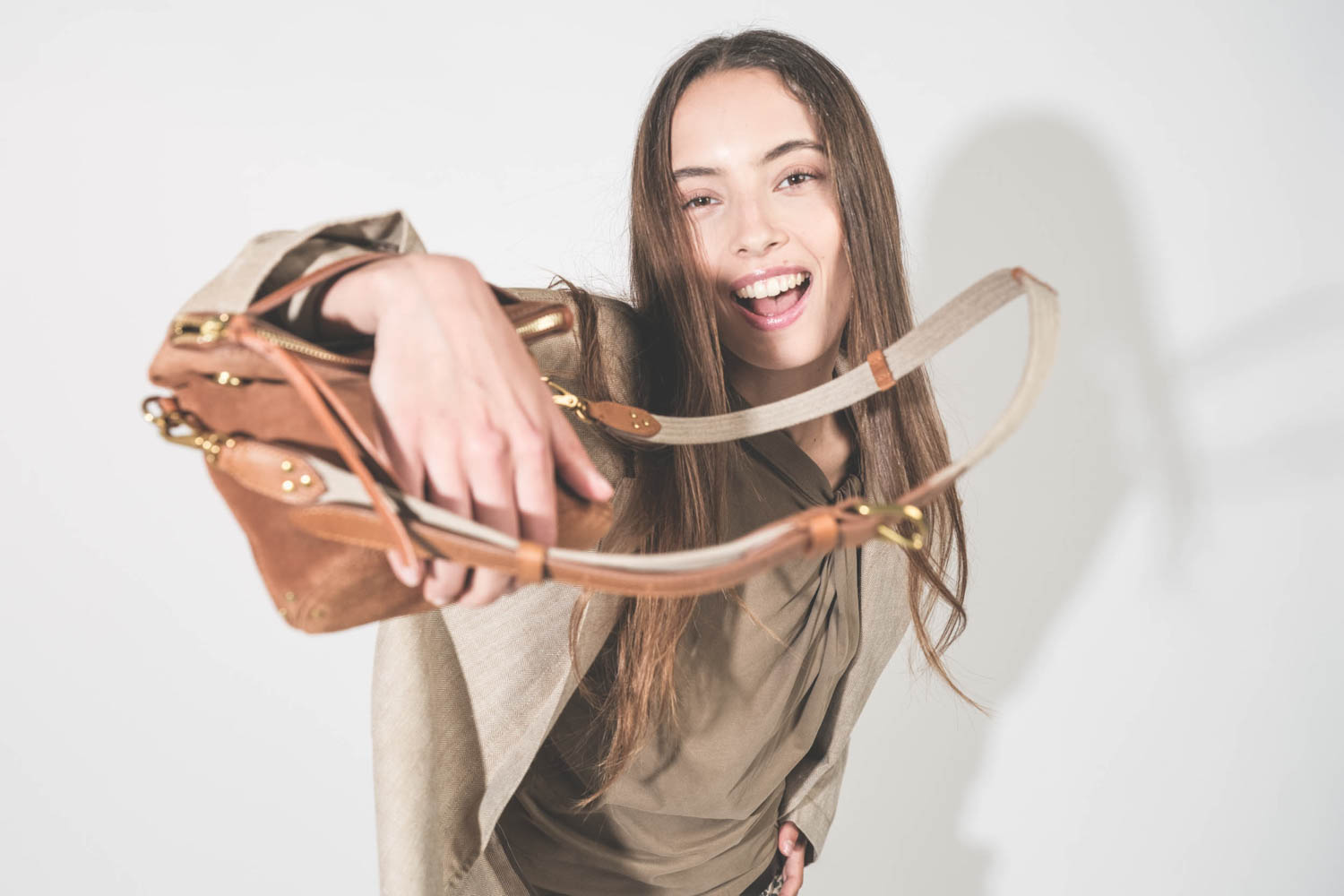 Pochette en cuir suédé caramel Lucky Jérôme Dreyfuss portée main avec une bandoulière sangle large écru Jérôme Dreyfuss. Alyssa porte une veste Ragged Oversized beige en lin R13 avec un tee-shirt sans manches Nayda kaki Isabel Marant Etoile. 