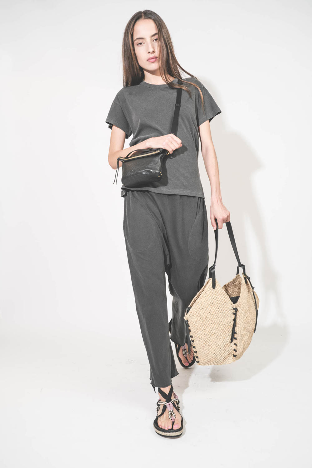 Pochette en cuir de chèvre noir grainé portée de face crossbody avec une bandoulière sangle large noire. Tee-shirt manches courtes Boxy Crew et pantalon sarouel en jersey noir délavé The Great. Sandales en cordes tressées et ruban noir Gypsa Isabel Marant