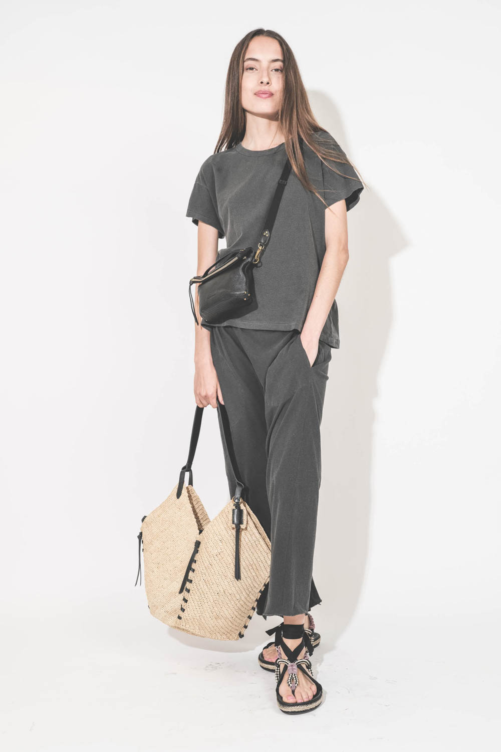Pochette en cuir de chèvre noir grainé portée crossbody avec une bandoulière sangle large noire Jérôme Dreyfuss. Tee-shirt manches courtes Boxy Crew et pantalon sarouel en jersey noir délavé The Great. Sandales en cordes tressées et ruban noir Gypsa Isabe