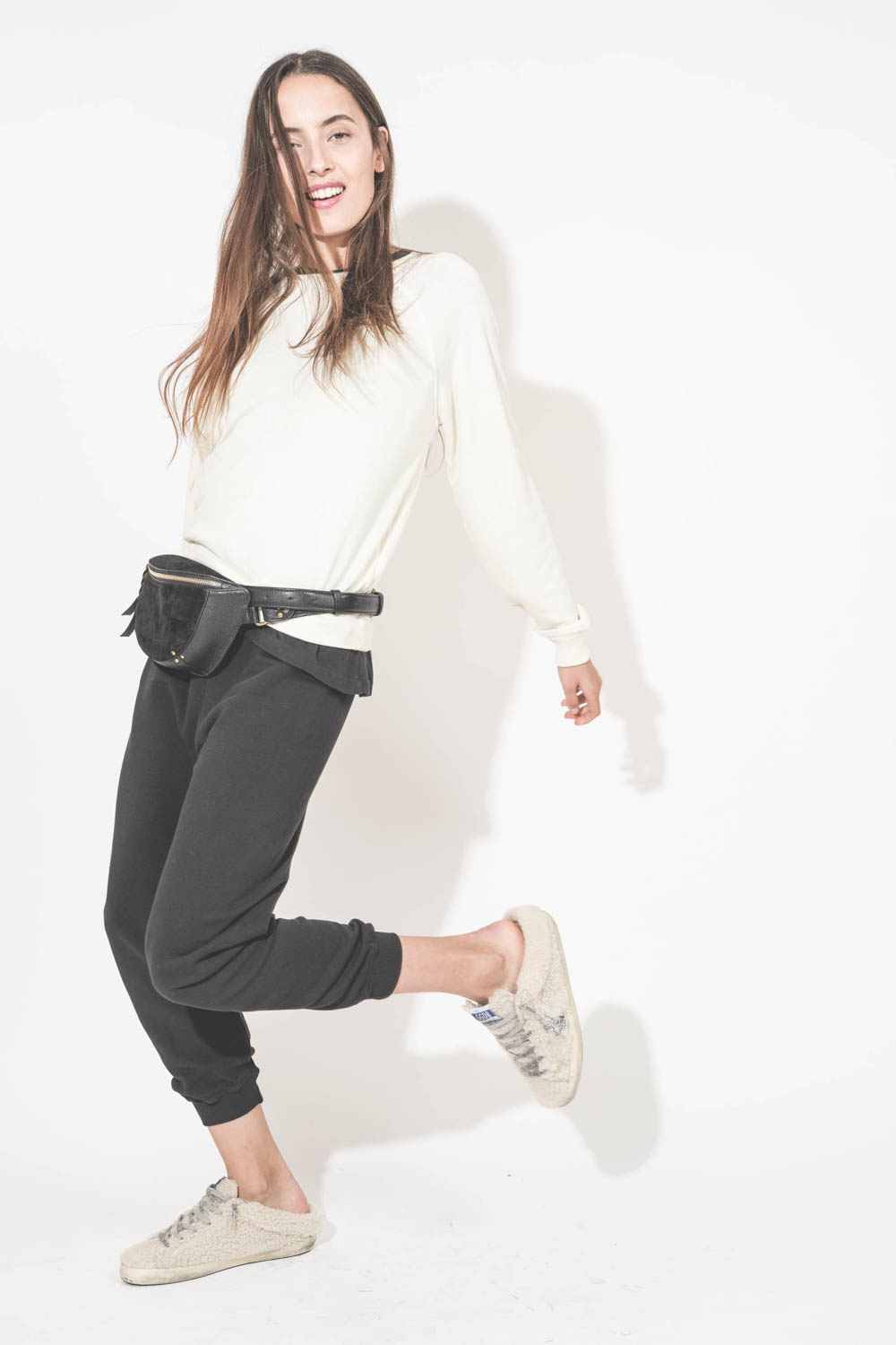 Sac banane en cuir chèvre grainé noir Lino Jérôme Dreyfuss. Porté à la taille avec un sweat-shirt écru Shrunken The Great et un pantalon de jogging court noir The Great. Sneakers Super Star sabot en Shearling écru Golden Goose.
