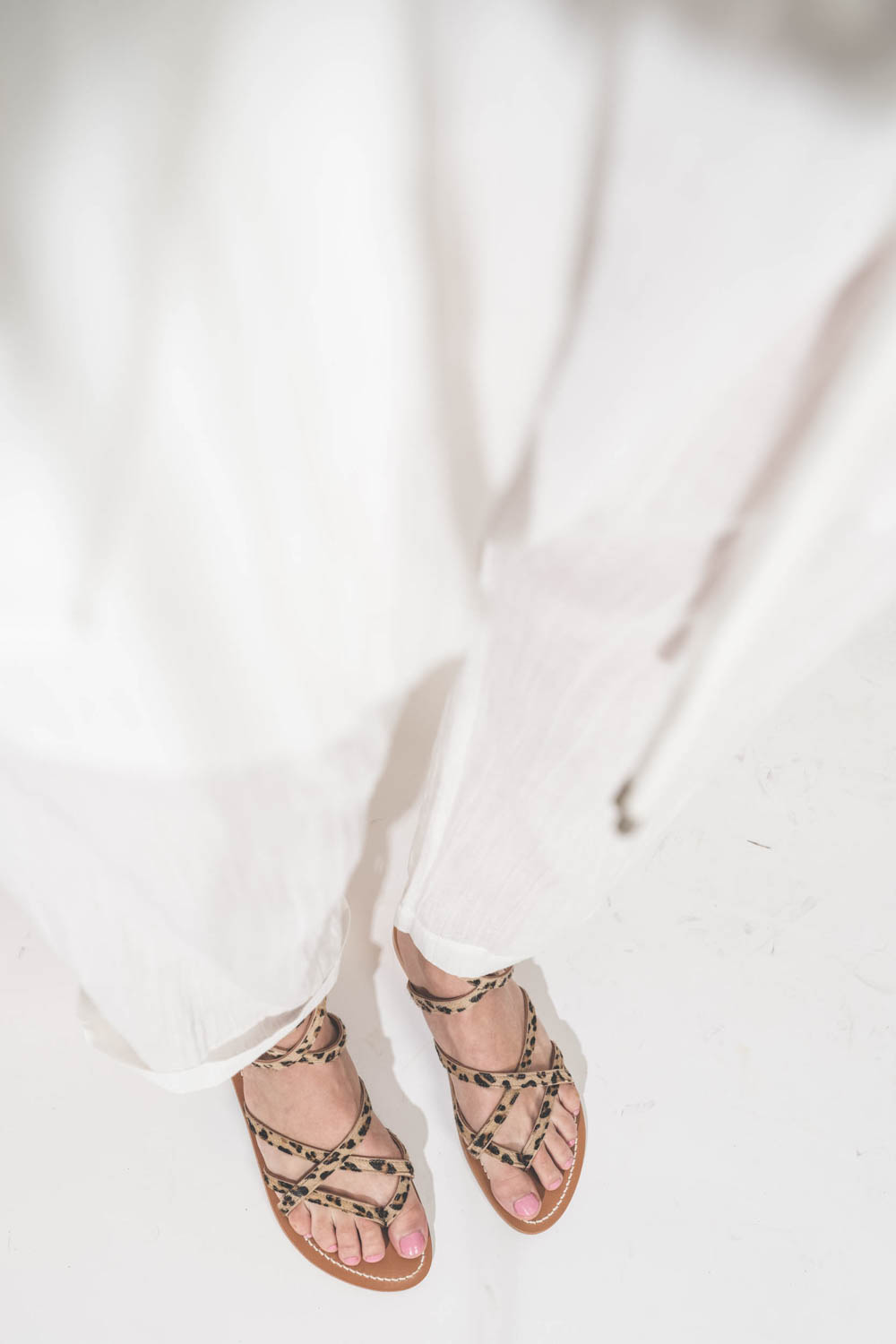 Sandales plates avec brides Zenobie K.Jacques St-Tropez en cuir "pony" léopard. Porté avec un pantalon en voile de coton blanc The Great.