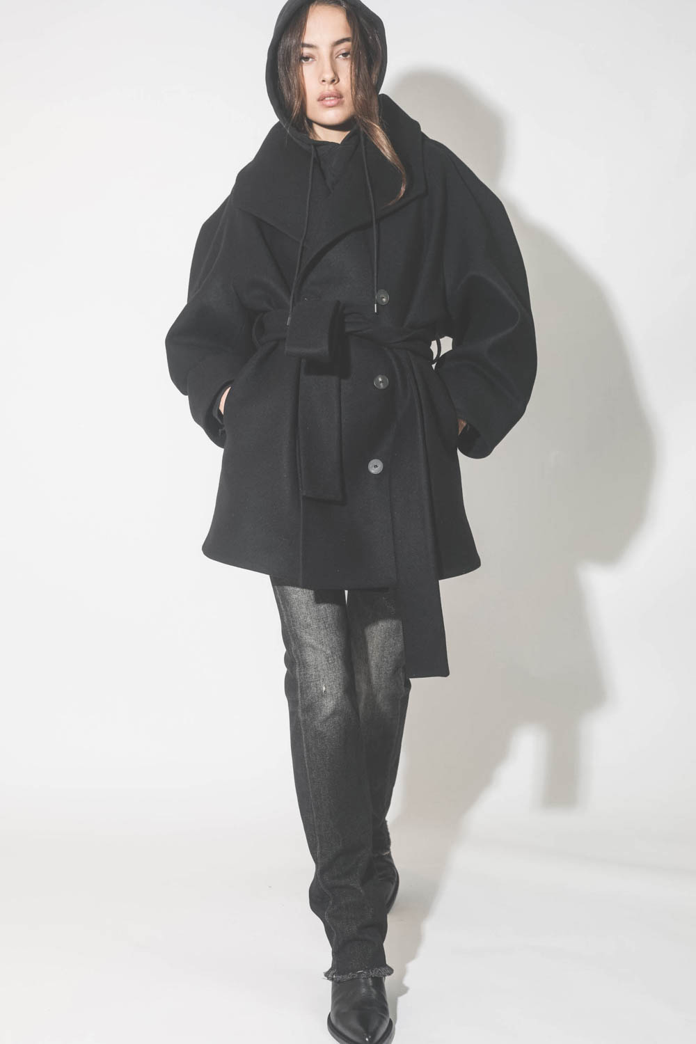 Manteau caban ceinturé en drap de laine noir Suzzane Vautrait. Porté avec un sweat-shirt à capuche noir.