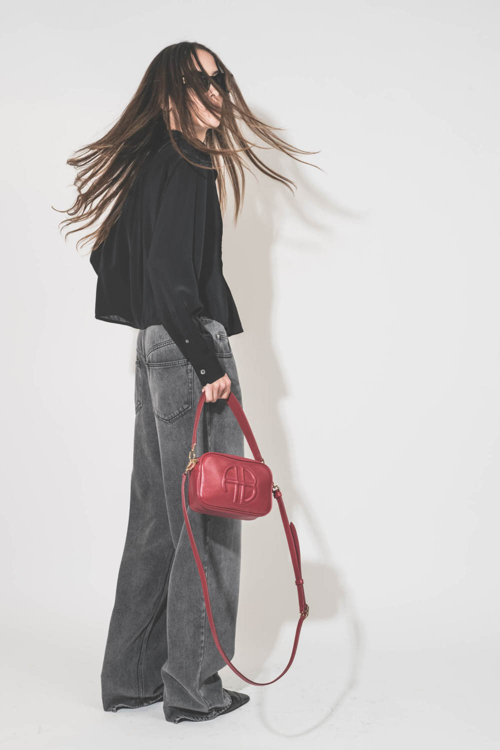 Jean large et fluide en Lyocell et coton gris clair Joanny Marant Etoile. Porté de profil dos avec un top en viscose noir Adzara Marant Etoile et des escarpins à talons en cuir noir Freya Anine Bing. Sac Lili rouge et lunettes de soleil montures noires In