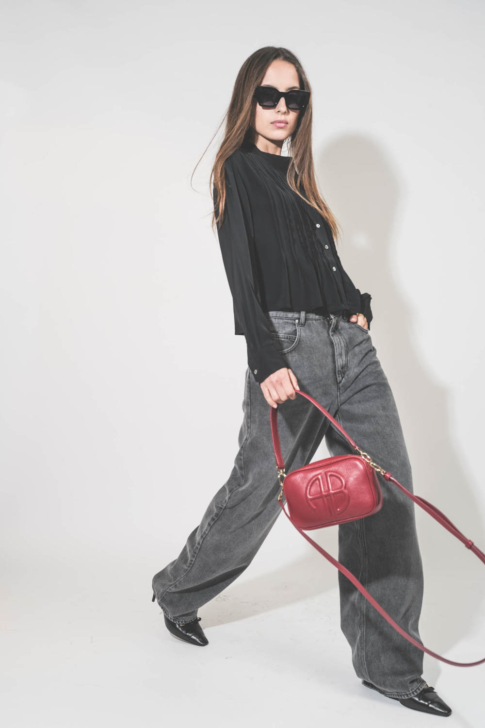 Jean large et fluide en Lyocell et coton gris clair Joanny Marant Etoile. Porté de profil avec un top en viscose noir Adzara Marant Etoile et des escarpins à talons en cuir noir Freya Anine Bing. Sac Lili rouge et lunettes de soleil montures noires Indio 