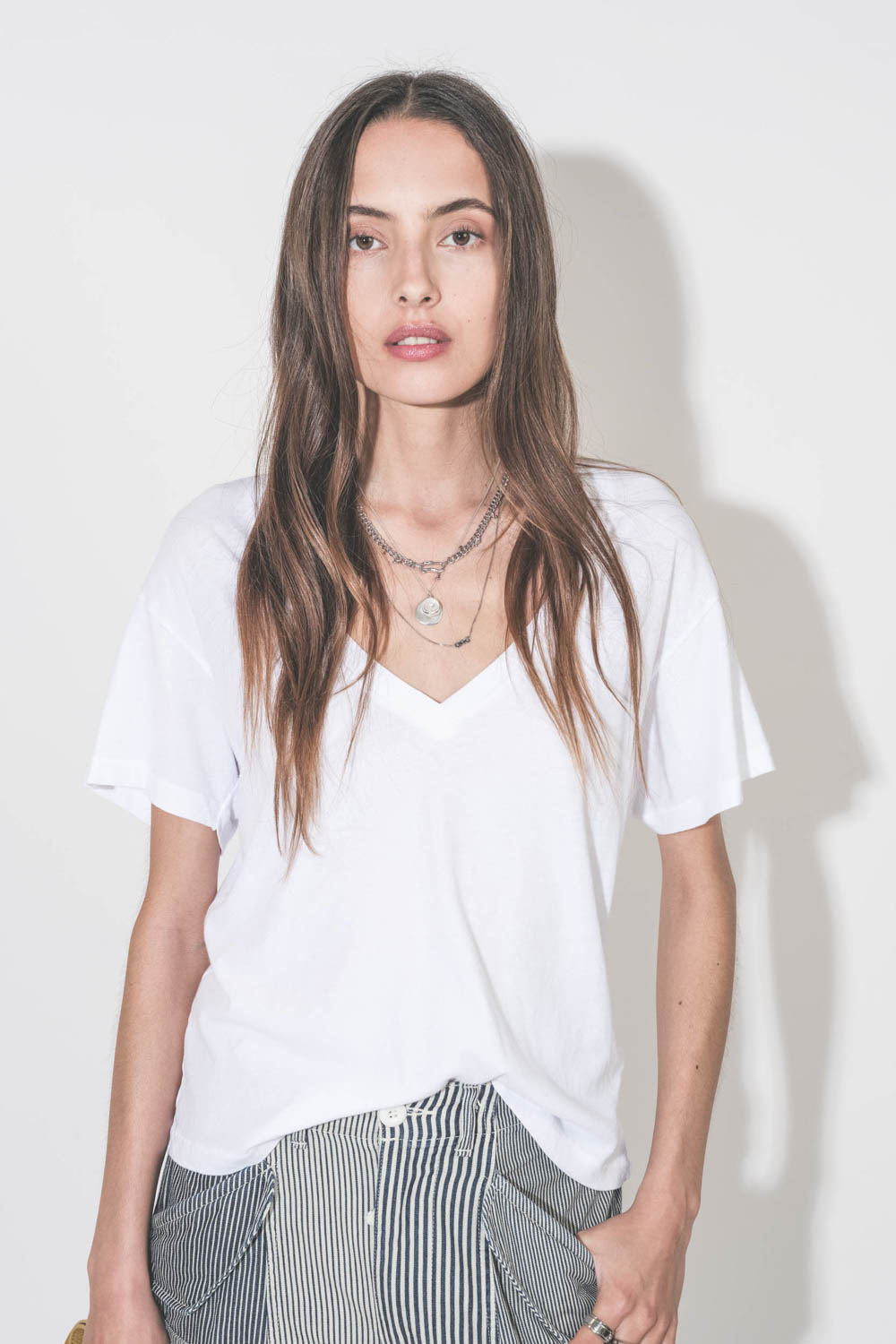 Collier long chaine avec lettre Dad en argent Maria Black. Porté en accumulation avec un collier chaine Berline en argent et un collier L'amour en argent Pascale Monvoisin. Tee-shirt blanc col V neck The Great.