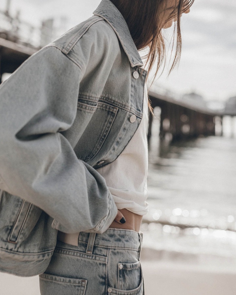 Blouson court oversize Mikuta en denim bleu clair, port&eacute; de profil.