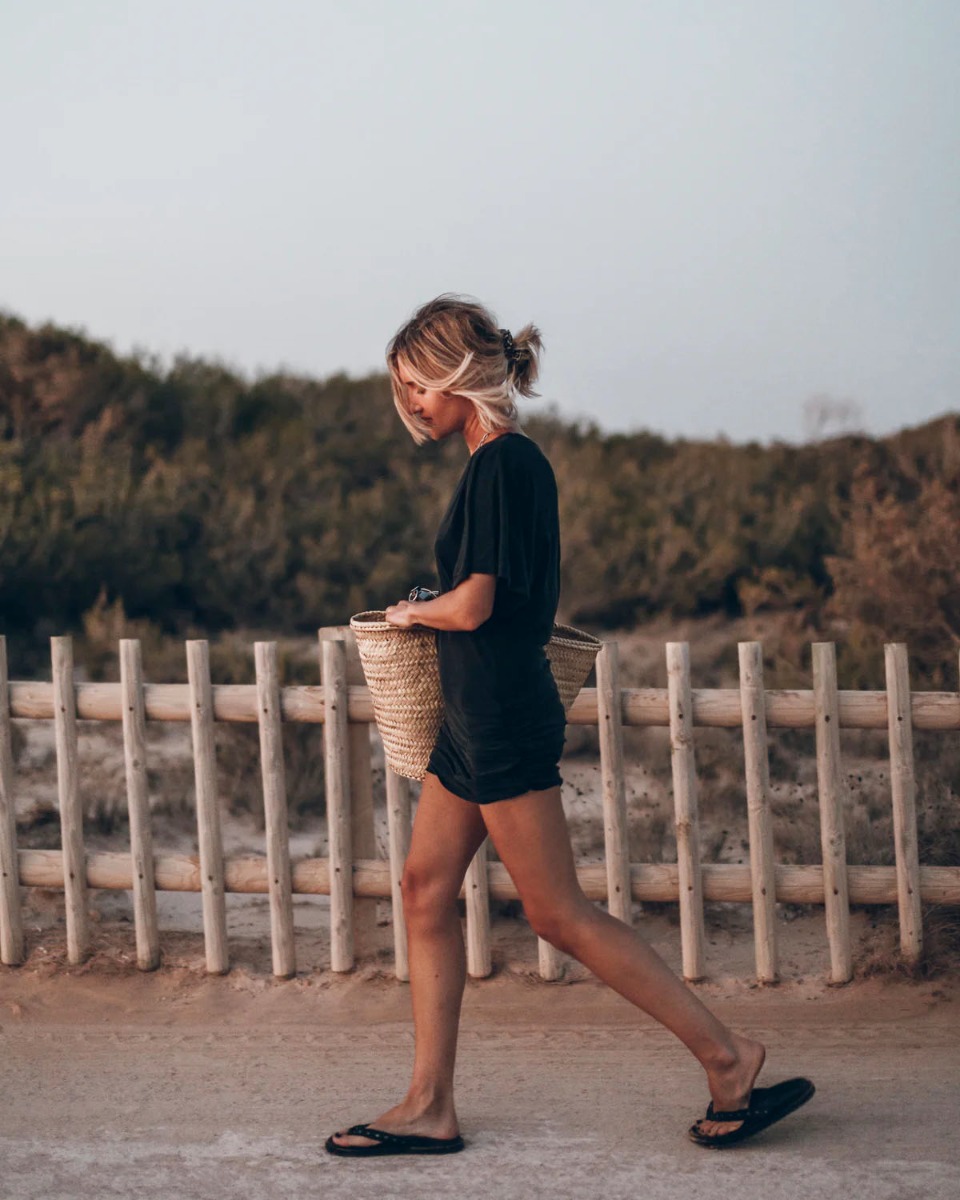 Robe courte drap&eacute;e Mikuta en jersey noir, port&eacute;e de profil avec un panier en osier.