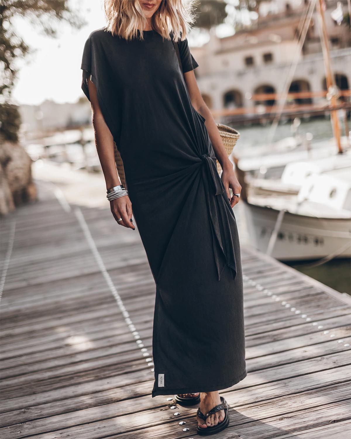 Robe longue manches chauve-souris à nouer à la taille ou sur le côté en Lyocell et coton fluide noire Mikuta. Portée de face avec des sandales noires.