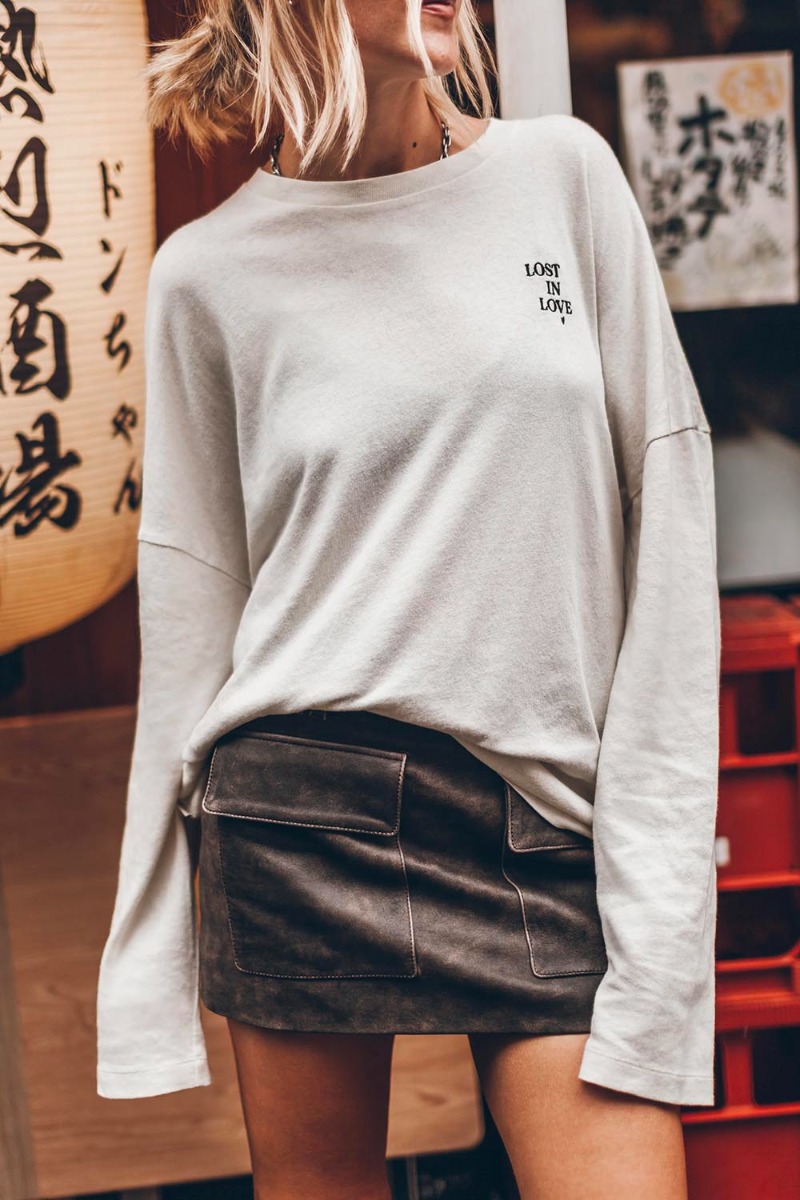 T-shirt Mikuta &agrave; manches longues en coton &eacute;cru, brod&eacute; " Lost In Love " sur la poitrine, port&eacute; de face avec une jupe en cuir Mikuta.