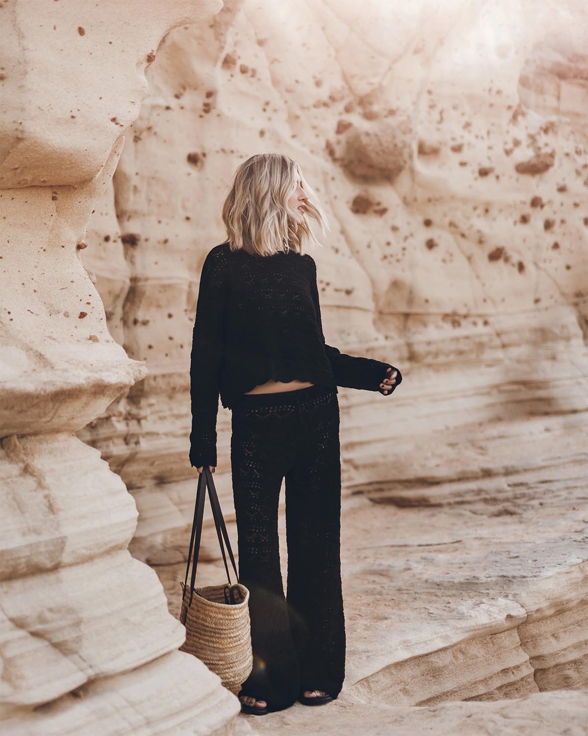 Pantalon en crochet noir en lin et coton Mikuta. Porté avec un pull en crochet noir assorti et un panier en osier.