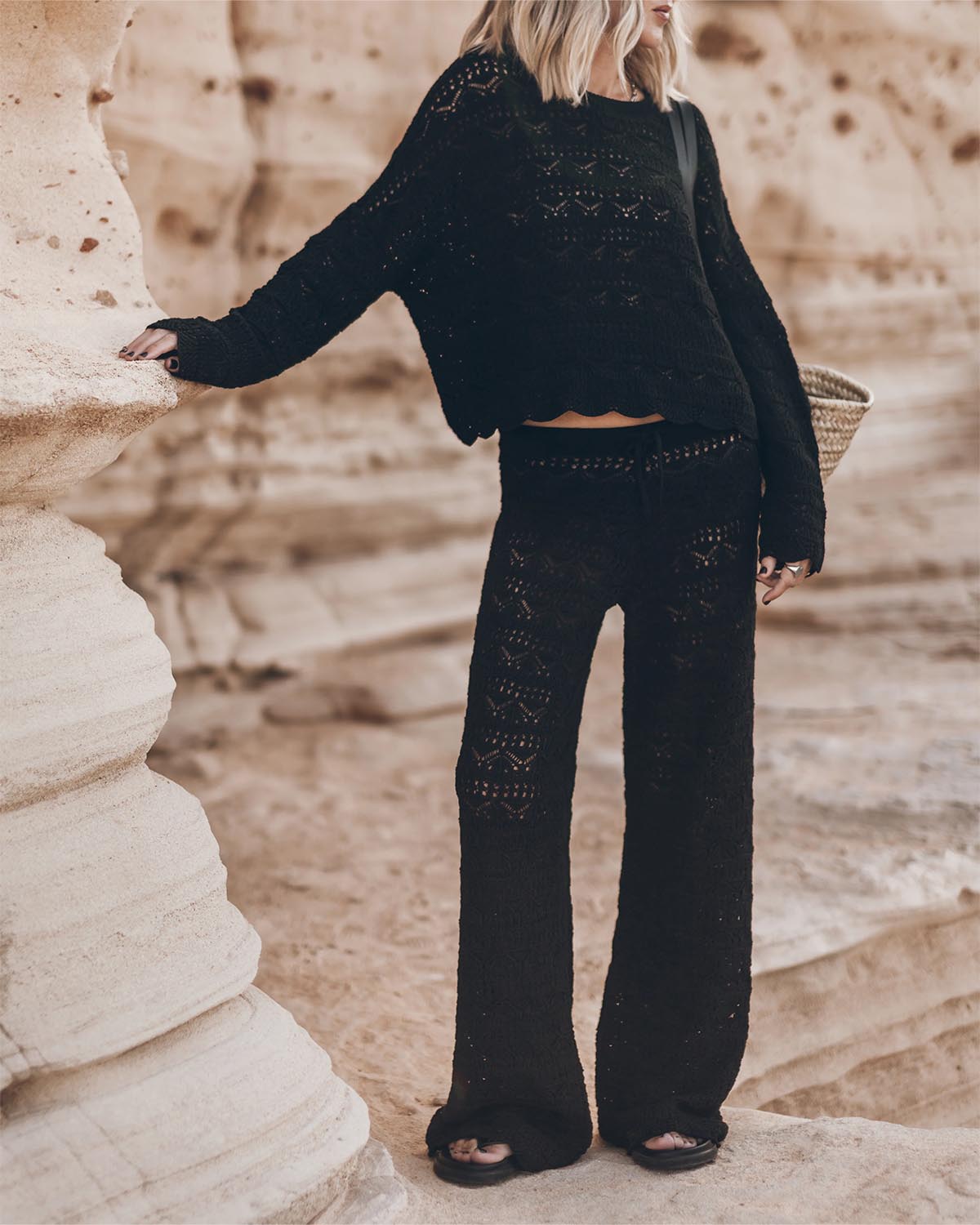 Pantalon taille basse en crochet noir en lin et coton Mikuta. Porté de face avec un pull assorti.