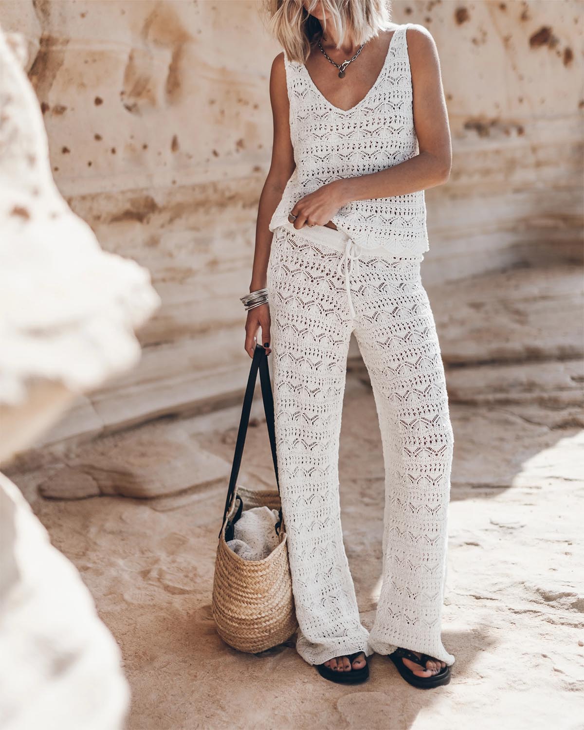 Pantalon en crochet écru en lin et coton Mikuta. Porté avec un débardeur en crochet écru assorti et un panier en osier.