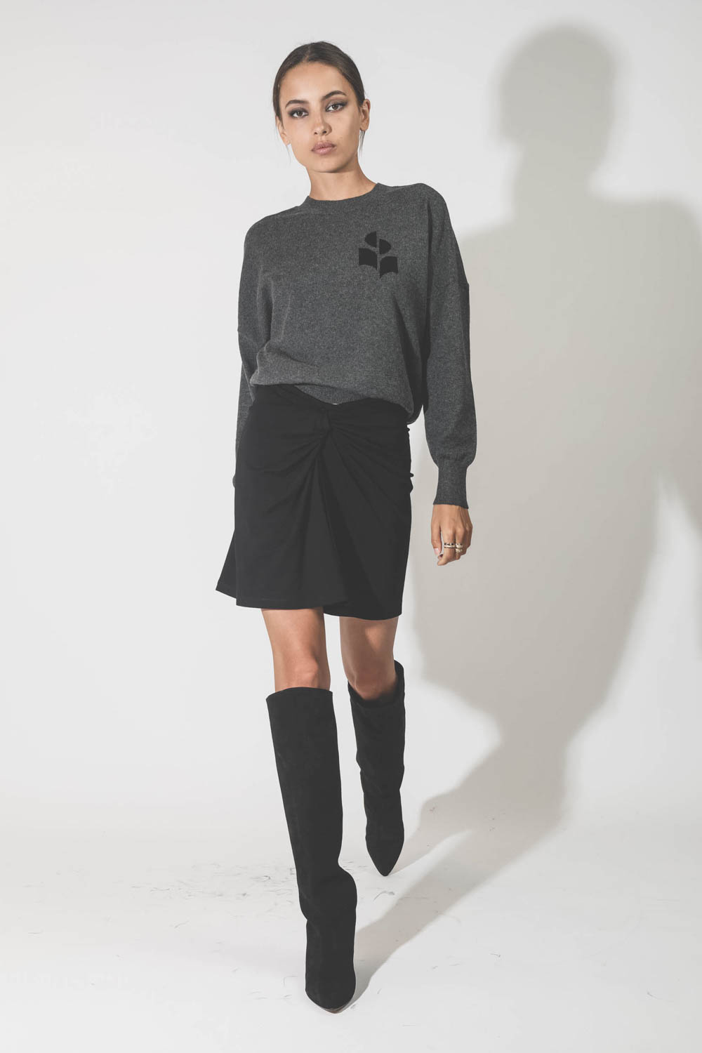 Mini-jupe en jersey noir drapé Natacha Marant Etoile. Porté avec des bottes en cuir suédé noir.