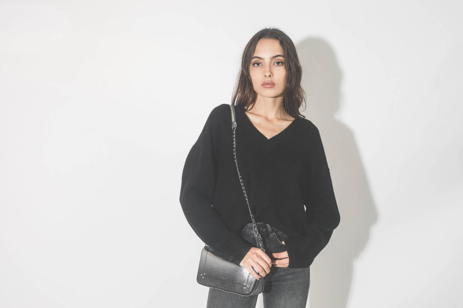 Pull col V en cachemire noir Lee Anine Bing. Port&eacute; avec un sac bandouli&egrave;re en cuir d&eacute;grad&eacute; argent.