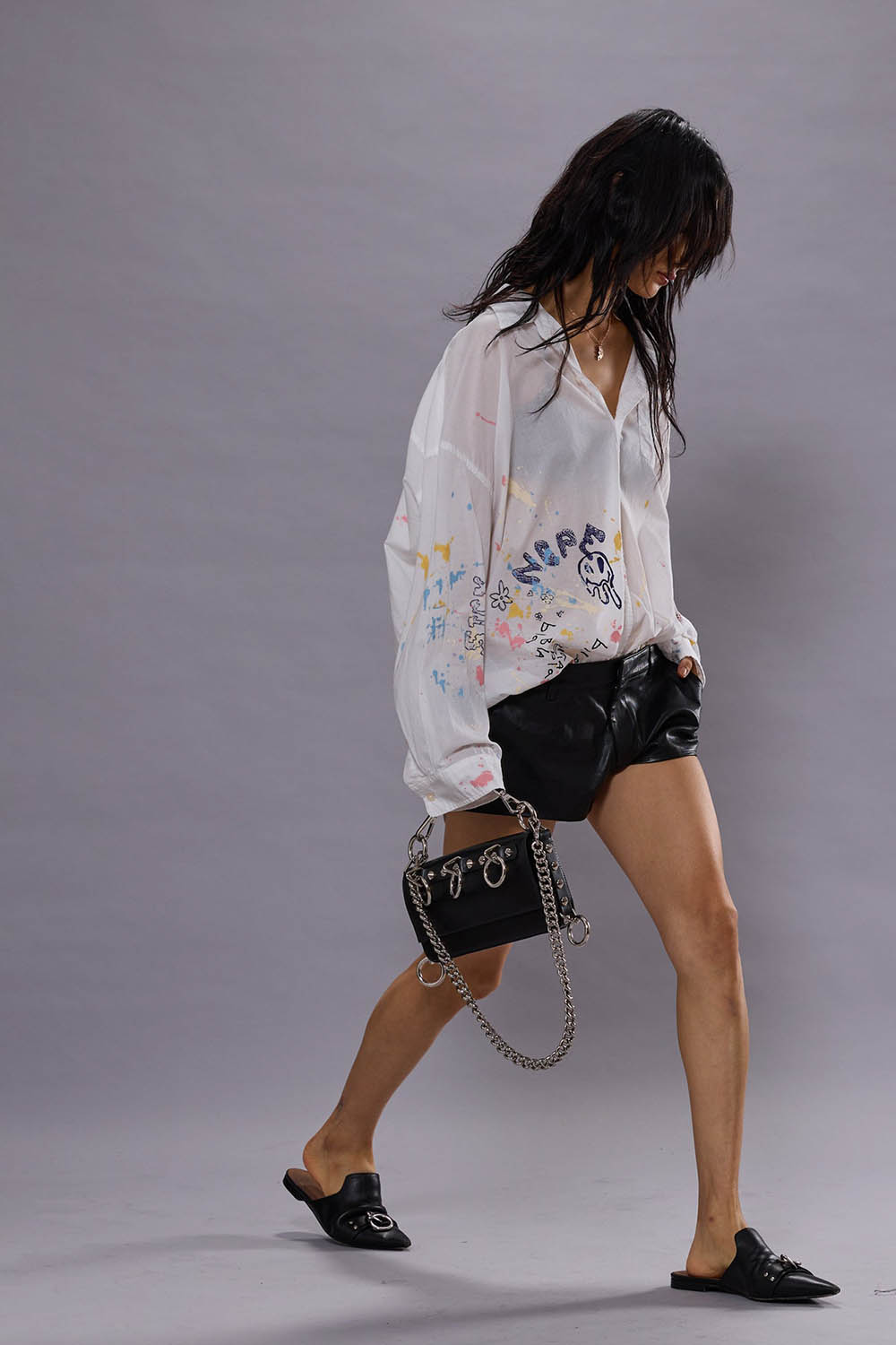 Produit Chemise manches longues oversize en coton blanc avec dessins esprit graffiti all over sur tout le bas de la chemise Drop Neck shirt R13. Porté de profil avec un mini-short en cuir noir.