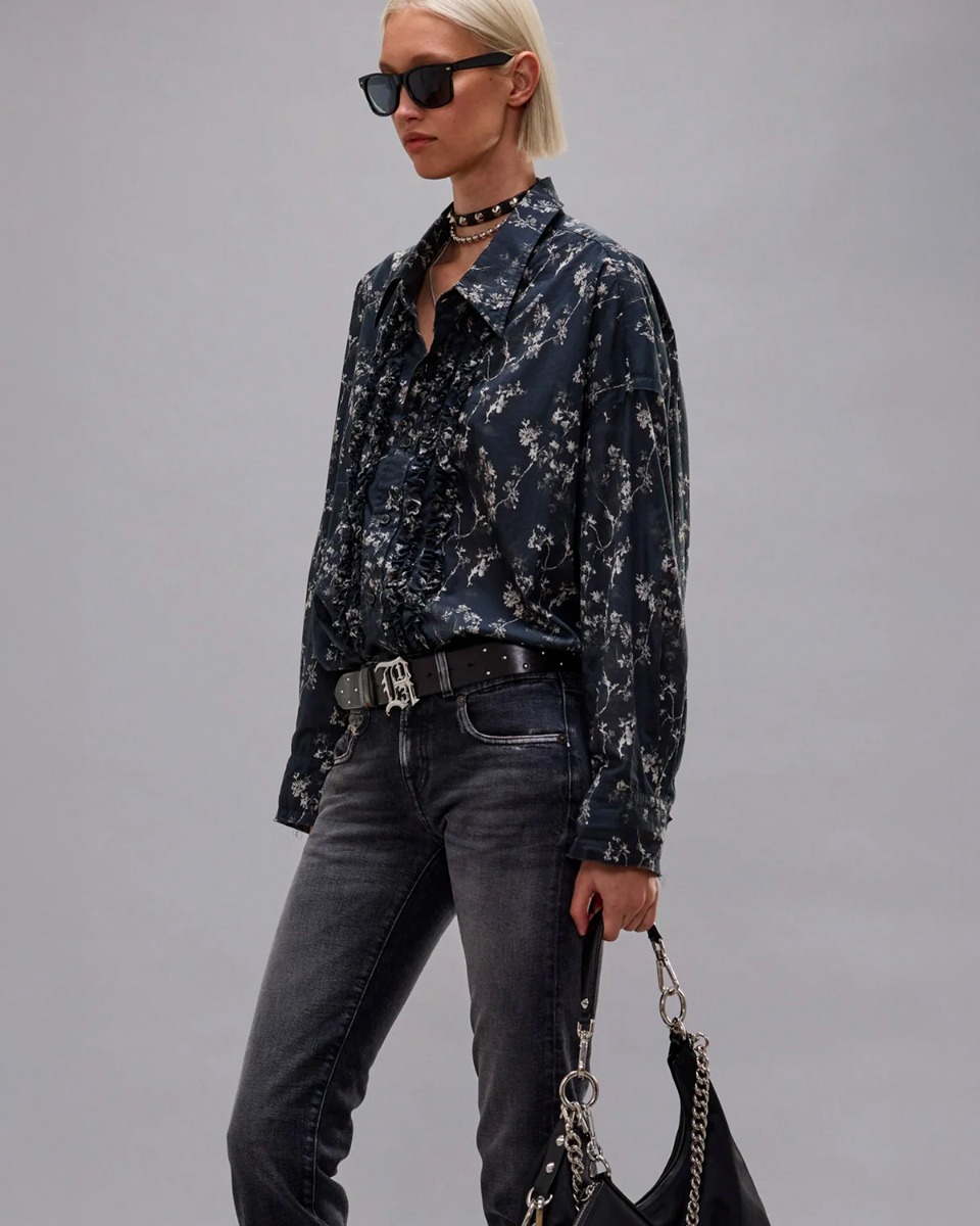 Chemise oversize &agrave; jabots R13 en voile de coton noir imprim&eacute; floral, port&eacute;e de profil rentr&eacute;e dans un jean noir.