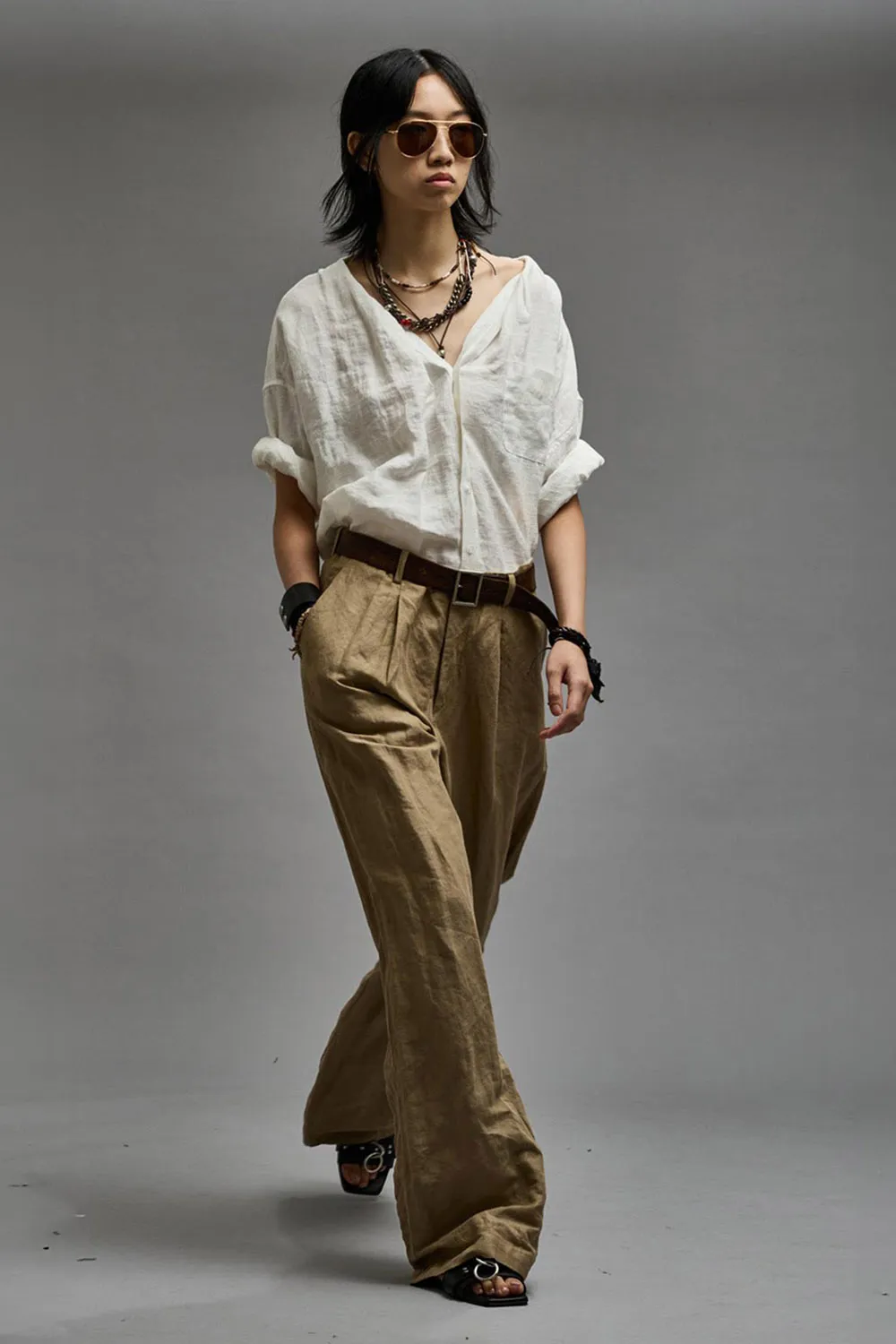 Chemise  froissée manches longues sans col en lin et viscose blanche Twisted Neck Shirt R13. Porté avec un pantalon beige.  