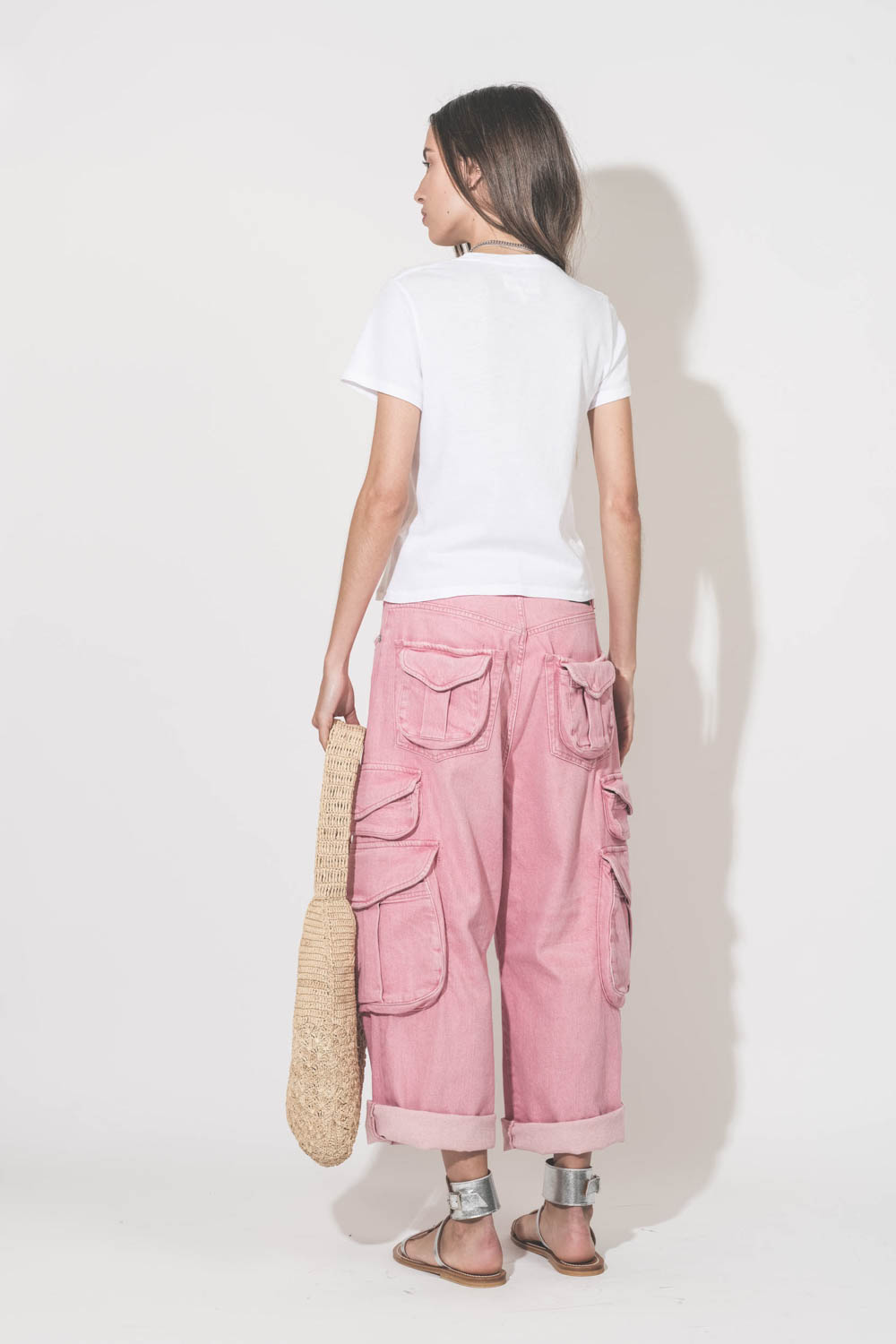 Jean taille basse oversized en toile rose multi-poches Cargo R13 denim. Porté de dos avec un tee-shirt blanc Little The Great, des sandales en cuir argent Caravelle K.Jacques St-Tropez et un sac en raphia naturel Praia Isabel Marant. 