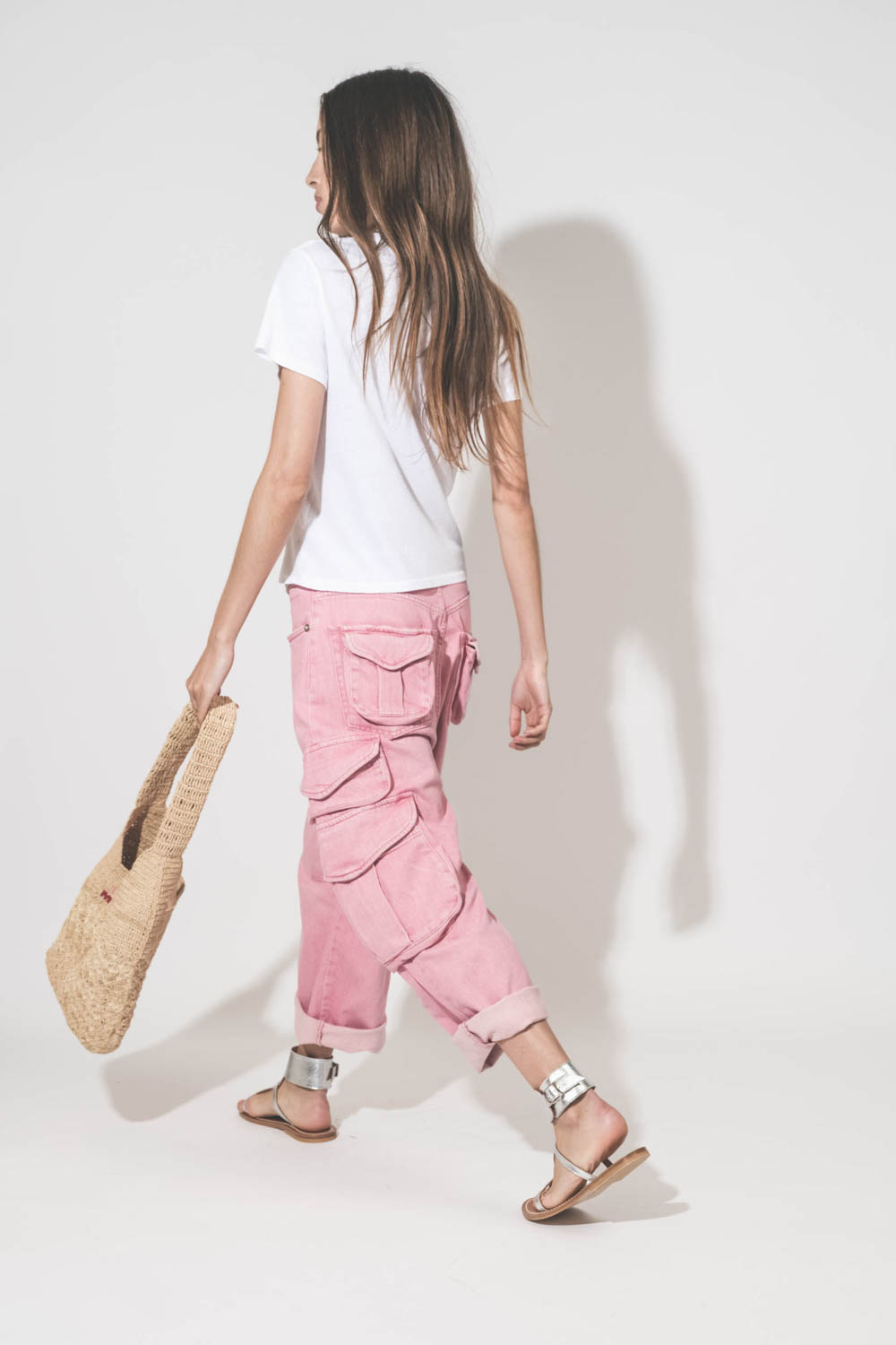 Jean taille basse oversized en toile rose multi-poches Cargo R13 denim. Porté de profil dos avec un tee-shirt blanc Little The Great, des sandales en cuir argent Caravelle K.Jacques St-Tropez et un sac en raphia naturel Praia Isabel Marant. 