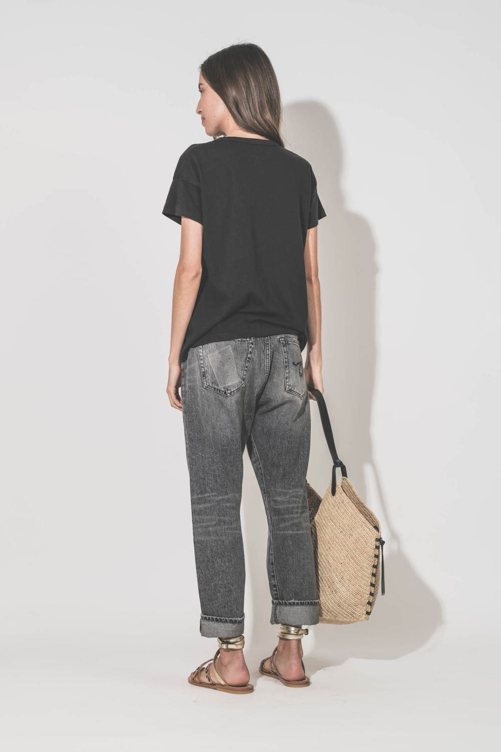 Jean Crossover Leyton Black R13 Denim. Porté de dos avec un tee-shirt manches courtes noir Boxy Crew The Great et des sandales plates en cuir naturel léopard platine K.Jacques Saint-Tropez. Ceinture en cuir noir Dara Isabel Marant et panier en osier natur