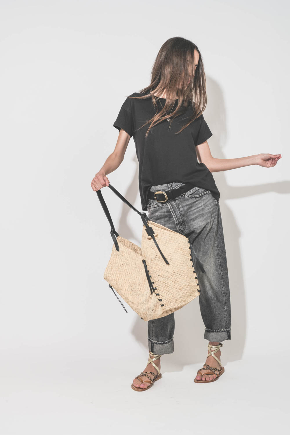Jean Crossover Leyton Black R13 Denim. Porté de face avec un tee-shirt manches courtes noir Boxy Crew The Great et des sandales plates en cuir naturel léopard platine K.Jacques Saint-Tropez. Ceinture en cuir noir Dara Isabel Marant et panier en osier natu