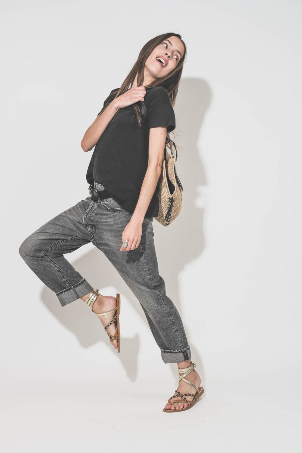 Jean Crossover Leyton Black R13 Denim. Porté de profil avec un tee-shirt manches courtes noir Boxy Crew The Great et des sandales plates en cuir naturel léopard platine K.Jacques Saint-Tropez. Ceinture en cuir noir Dara Isabel Marant et panier en osier na