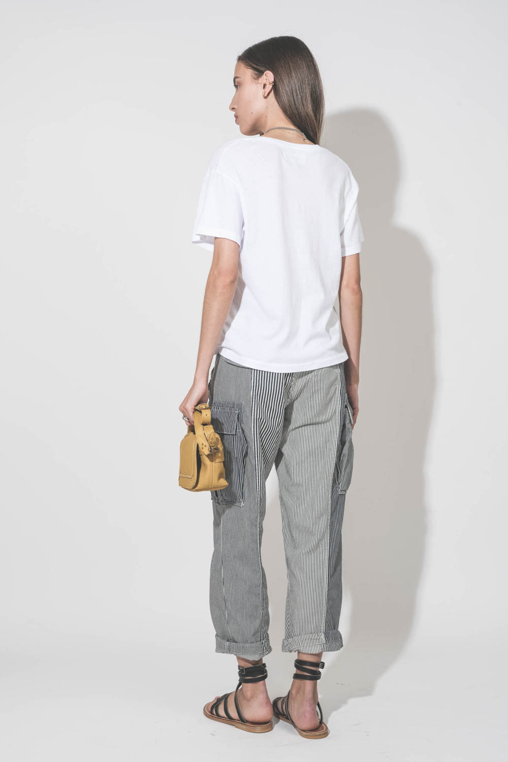 Pantalon oversize à rayures bleues Cargo Railroad R13. Porté de dos avec un tee-shirt blanc col V The Great, des sandales plates en cuir noir Zenobie K.Jacques Saint-Tropez et un sac Pepito S jaune Mimosa Jérôme Dreyfuss. 