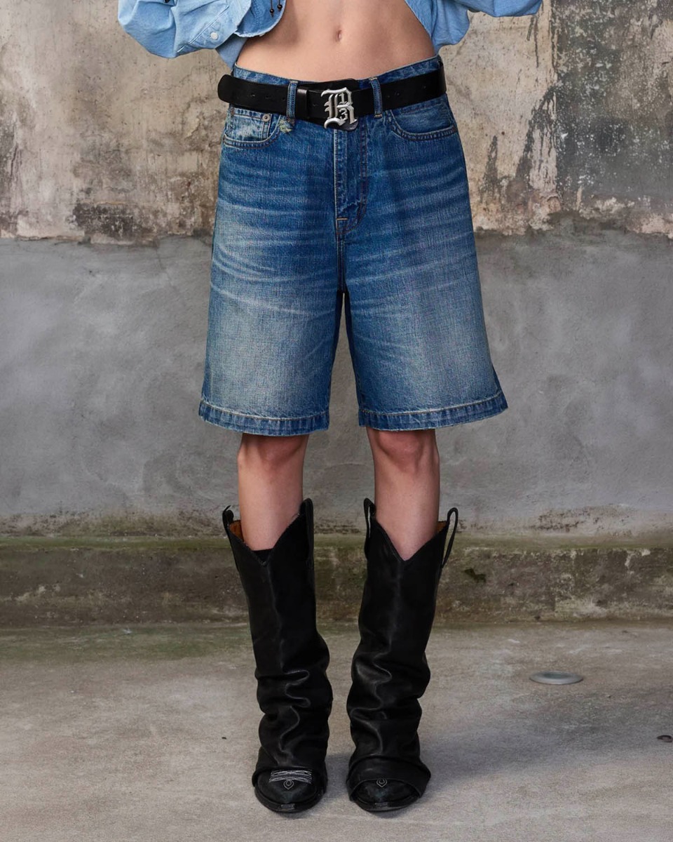 Short bermuda Relaxed R13 en denim bleu d&eacute;lav&eacute; &laquo; Depot Blue &raquo;, port&eacute; de face avec une ceinture.