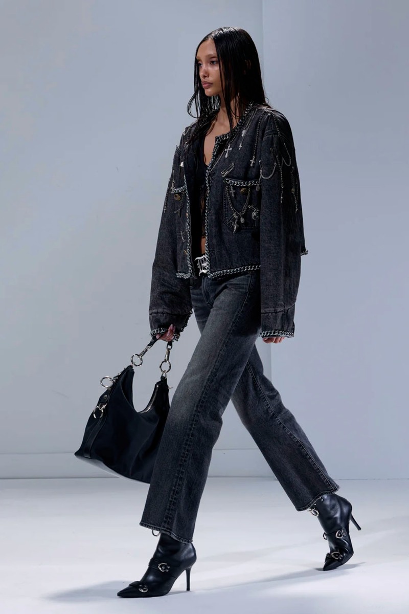 Produit Veste courte Chain Embellished Cropped Chore Jacket R13 en denim gris foncé, customisée avec des chaînes, des épingles à nourrice et des médailles en métal argenté. Portée avec un jean noir délavé R13.