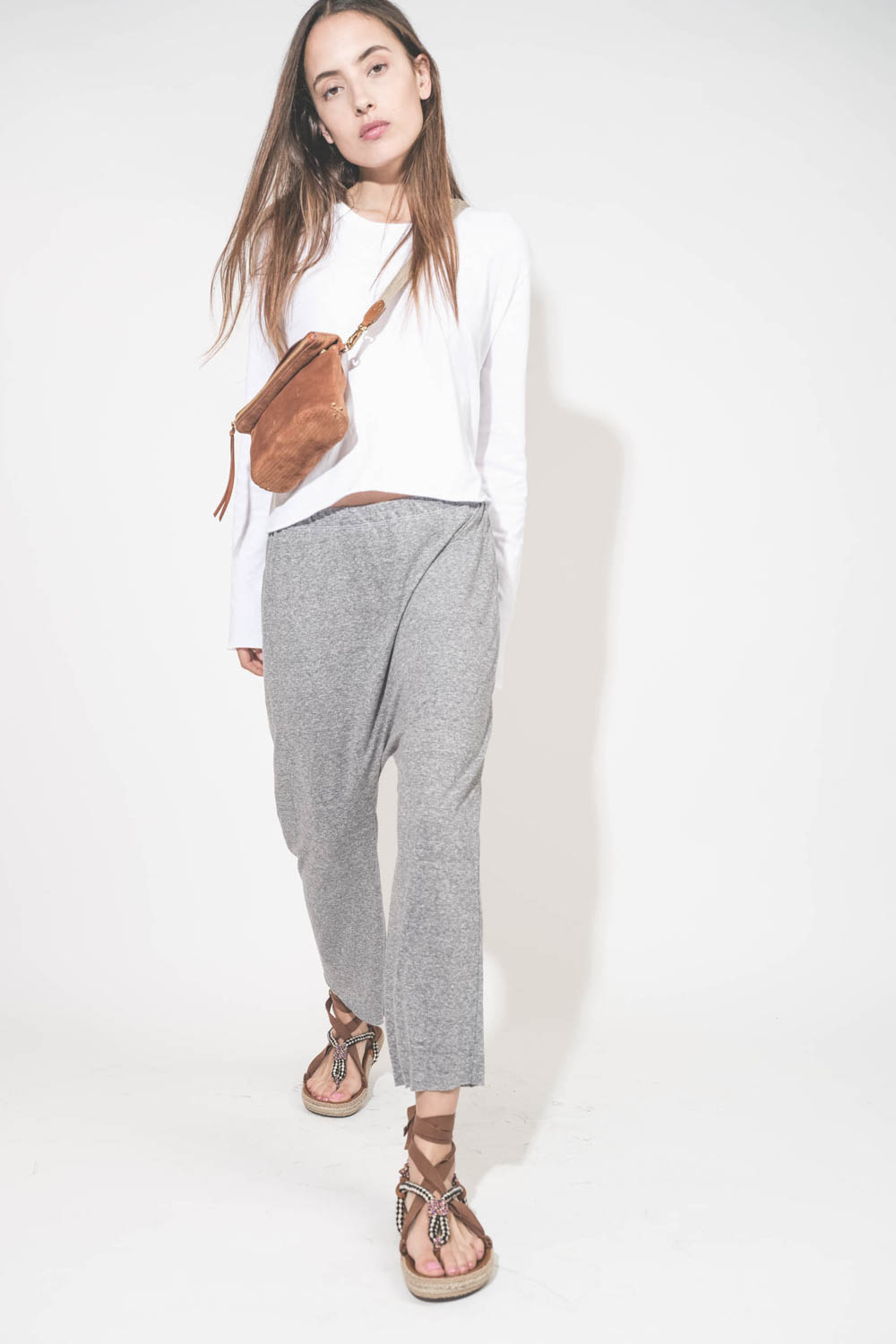 Pantalon sarouel court en jersey gris chiné The Great. Porté avec une tee-shirt court manches longues blanc et des sandales en cordes tressées et ruban beige Gypsa Isabel Marant. Pochette Lucky en cuir suédé caramel portée crossbody avec une sangle large 