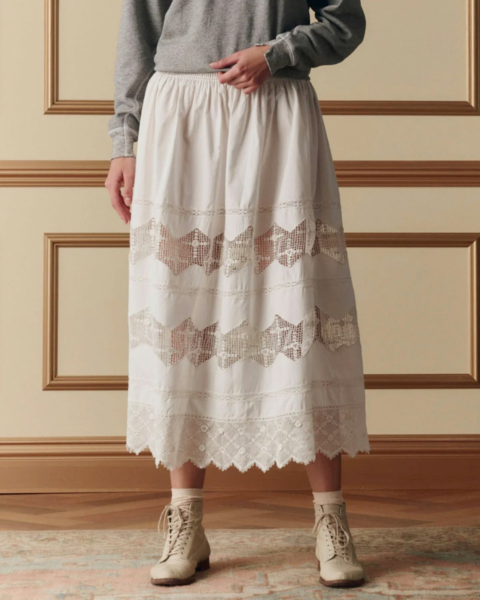 Jupe longue Rosette Crochet The Great en coton et dentelle blanche, port&eacute;e de face avec un sweat-shirt gris chin&eacute;.