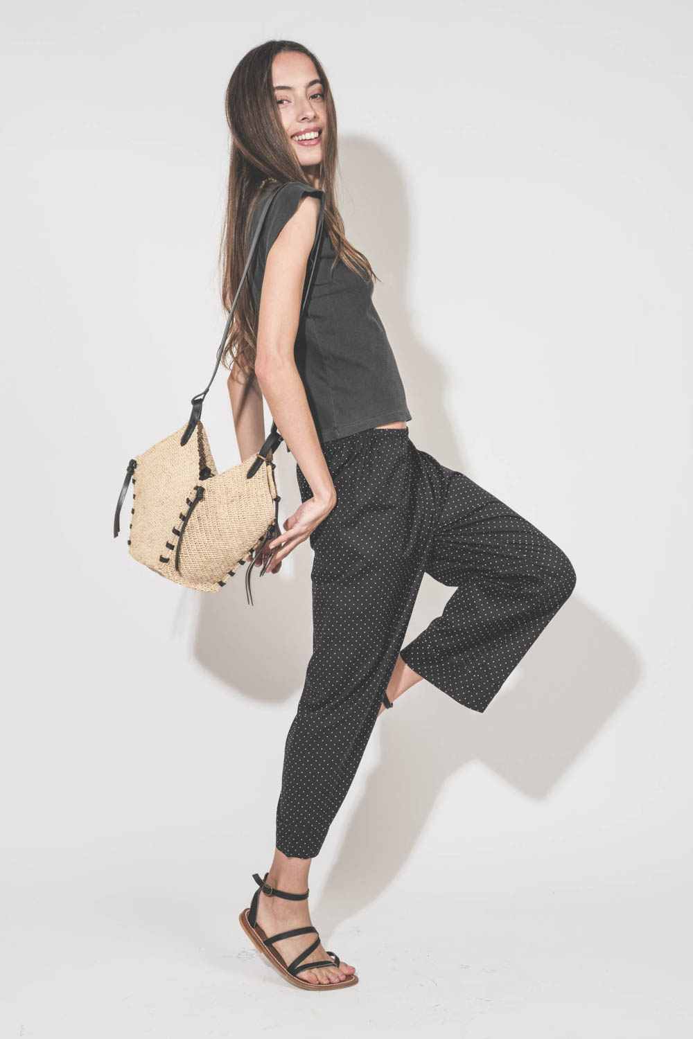 Pantalon taille basse en voile de coton noir à pois blancs Easy Sleep The Great. Porté de profil avec un tee-shirt sans manches noir Peak Shoulder The Great et des sandales en cuir noires Zenobie K.Jacques St-Tropez. Panier en osier bandoulière en cuir no