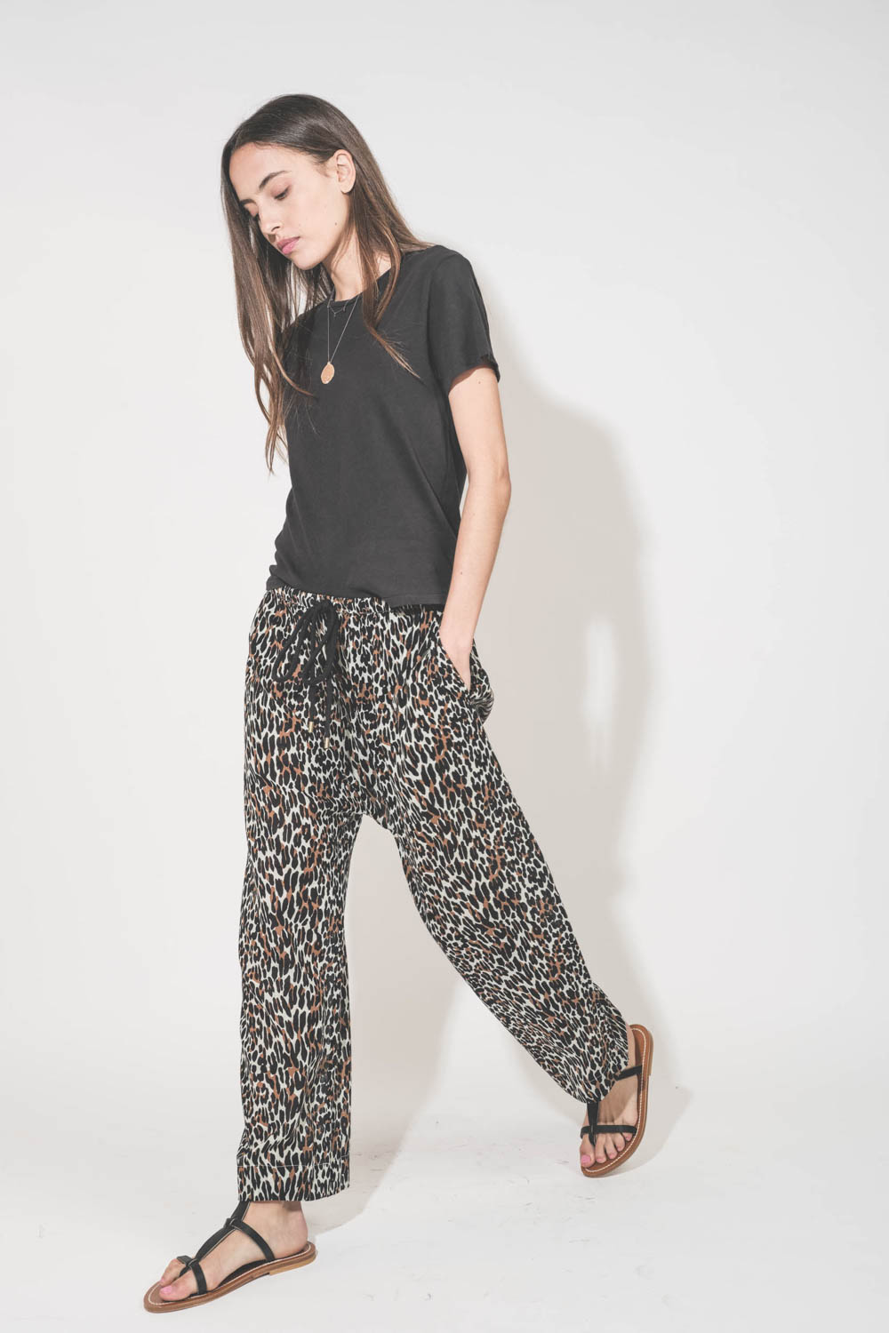 Pantalon Sarouel en voile de coton imprimé léopard Reef The Great. Porté de profil avec une tee-shirt manches courtes noir Boxy Crew The Great et des sandales en cuir noir Artimon K.Jacques St-Tropez. Collier en or jaune et diamants Rio et Palerme Pascale