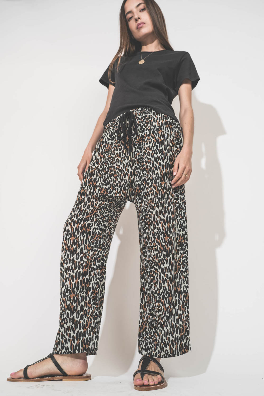 Pantalon Sarouel en voile de coton imprimé léopard Reef The Great. Porté de face avec une tee-shirt manches courtes noir Boxy Crew The Great et des sandales en cuir noir Artimon K.Jacques St-Tropez. Collier en or jaune et diamants Rio et Palerme Pascale M