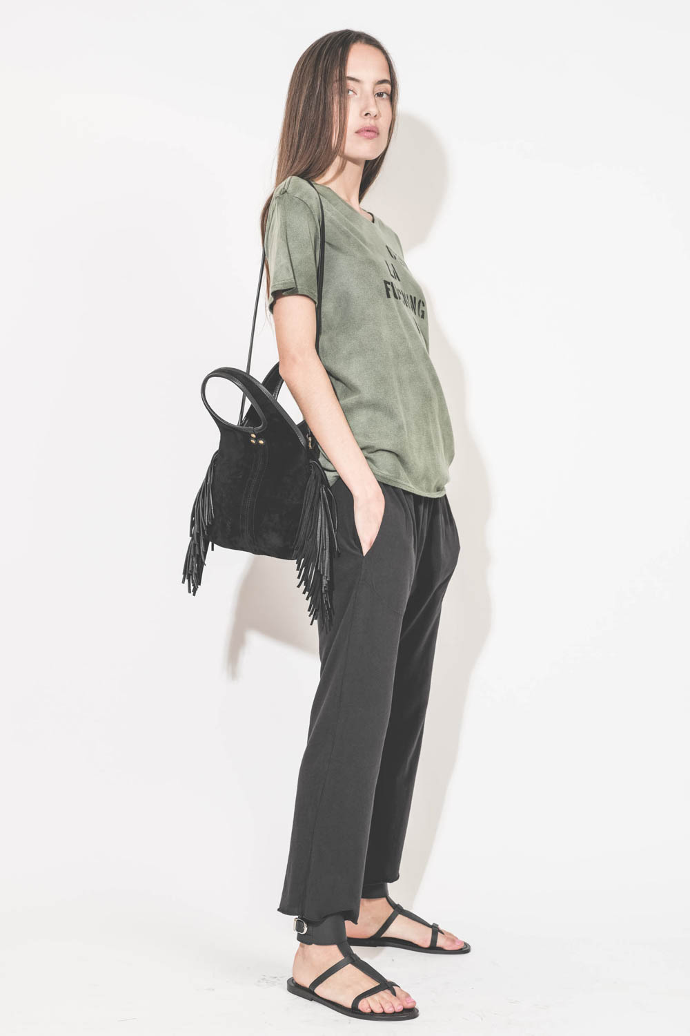Pantalon sarouel court en jersey noir The Great. Porté de profil avec un tee-shirt manches courtes à message "C'est la Fucking Vie" R13 et des sandales en cuir noir Ebene semelles noires Caravelle K.Jacques St-Tropez. Mini-sac en cuir suédé à franges noir