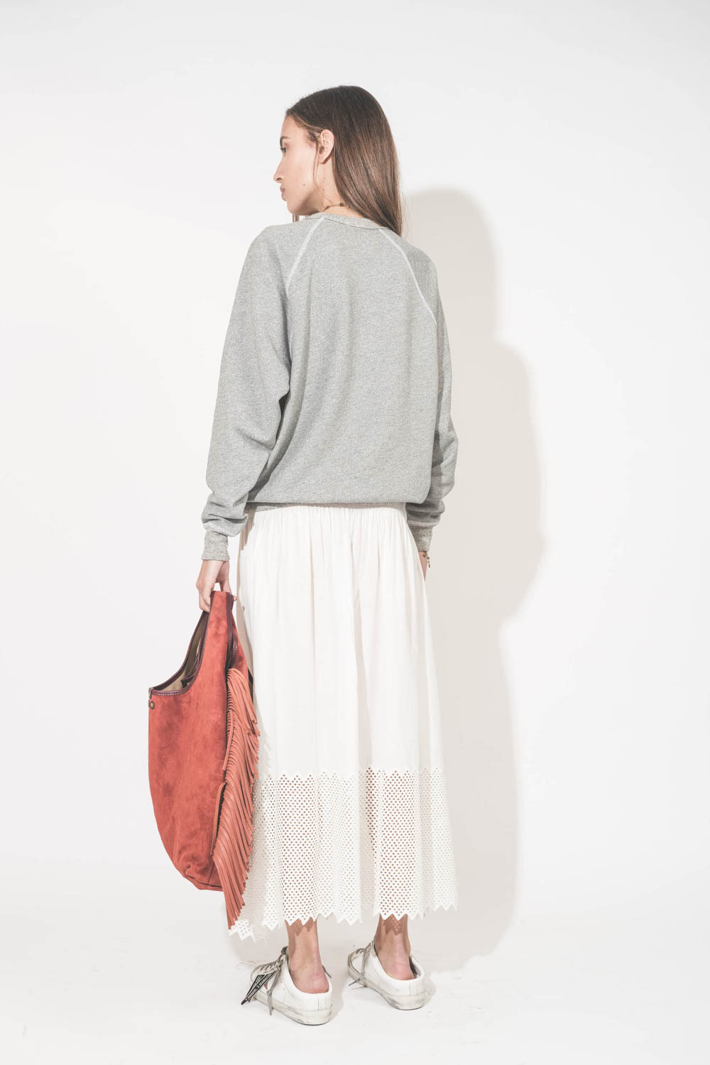 Sweat-shirt classique manches longues col rond col rond surpiqures contrastées blanches College The Great. Porté de dos avec une jupe longue en coton blanc The Great et des sneakers Super Star sabot Golden Goose. Sac à franges Paco Terracotta Jérôme Dreyf