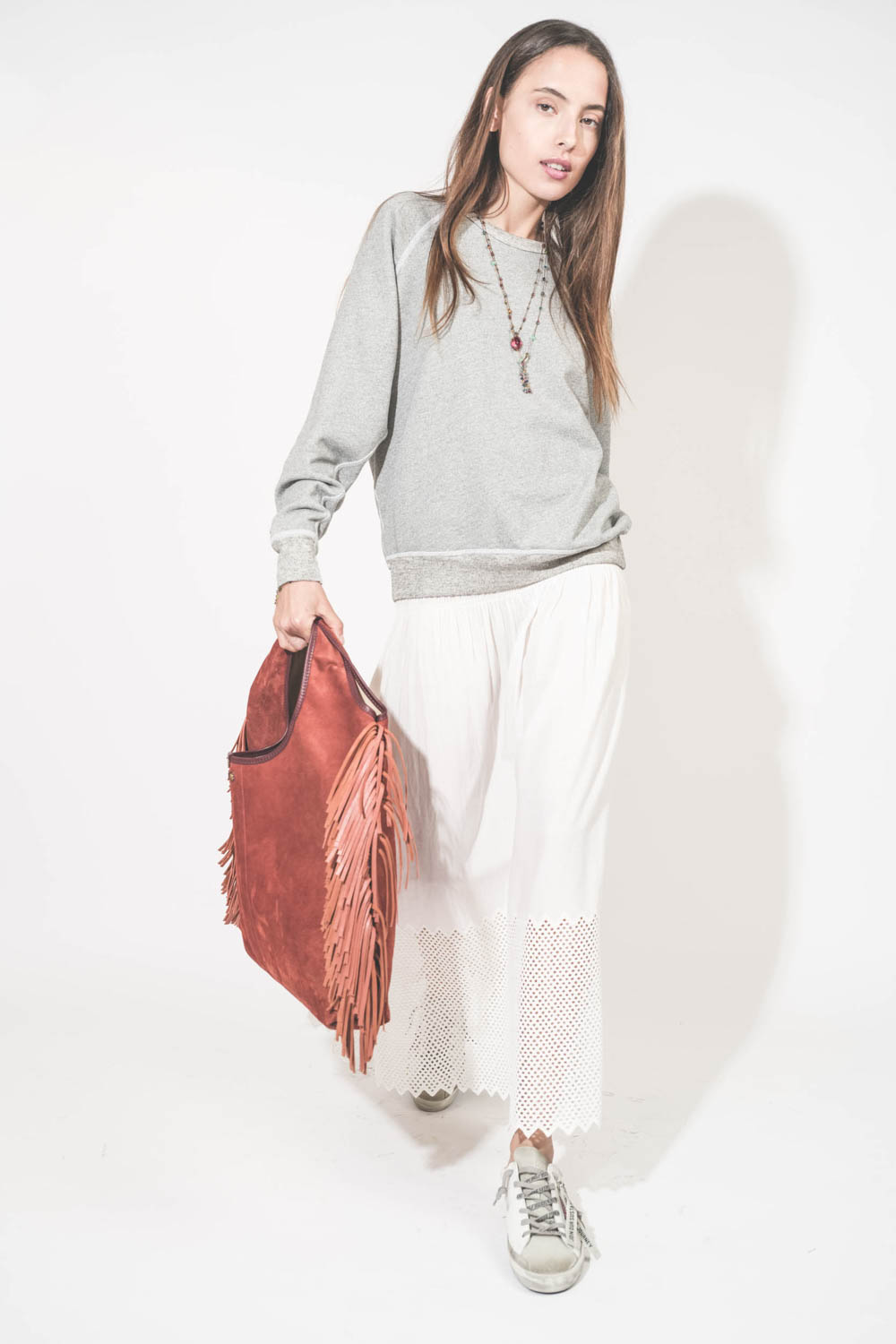 Sweat-shirt classique manches longues col rond col rond surpiqures contrastées blanches College The Great. Porté en marchant avec une jupe longue en coton blanc The Great et des sneakers Super Star sabot Golden Goose. Sac à franges Paco Terracotta Jérôme 