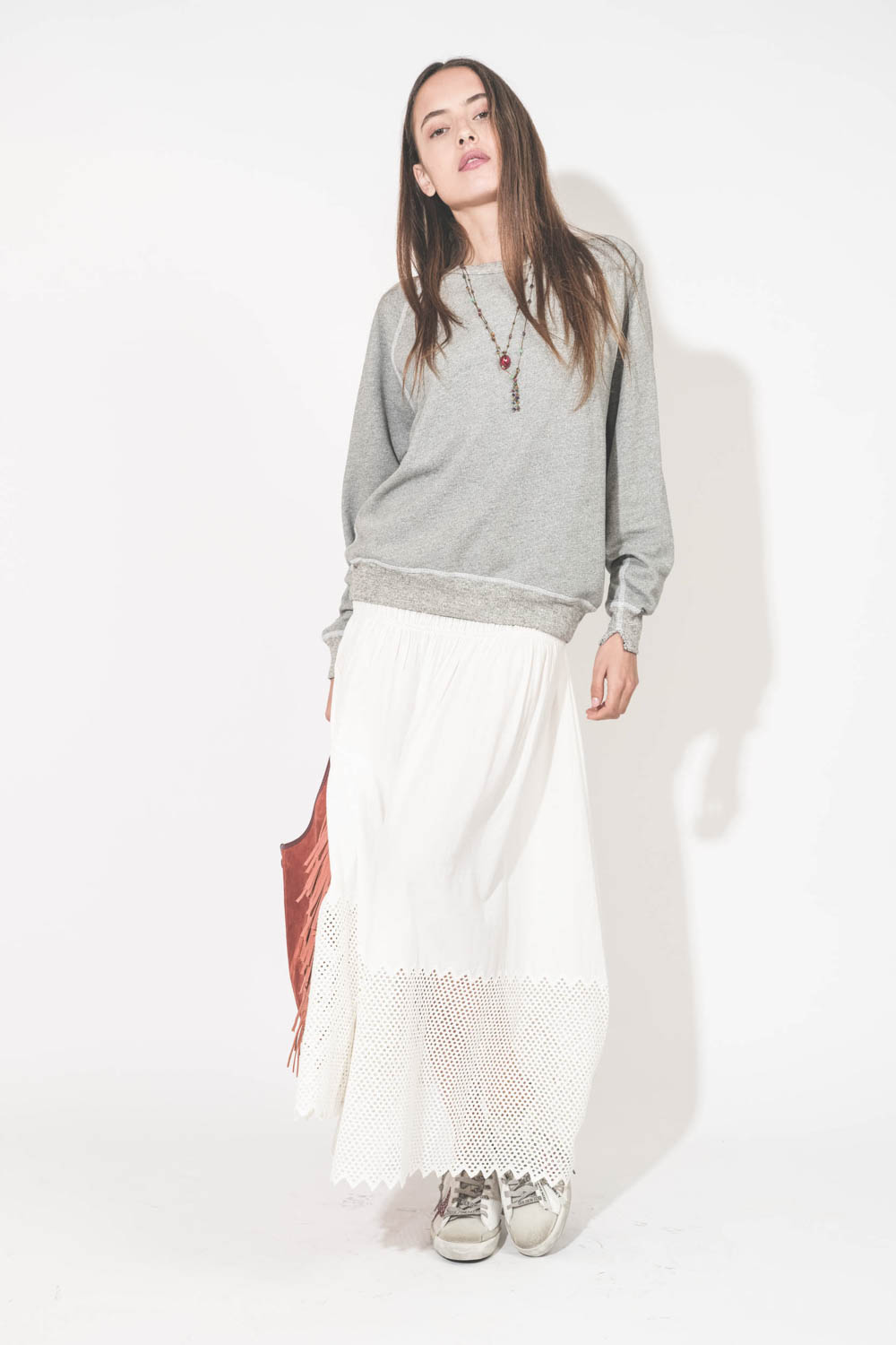 Sweat-shirt classique manches longues col rond col rond surpiqures contrastées blanches College The Great. Porté de face avec une jupe longue en coton blanc The Great et des sneakers Super Star sabot Golden Goose. Sac à franges Paco Terracotta Jérôme Drey