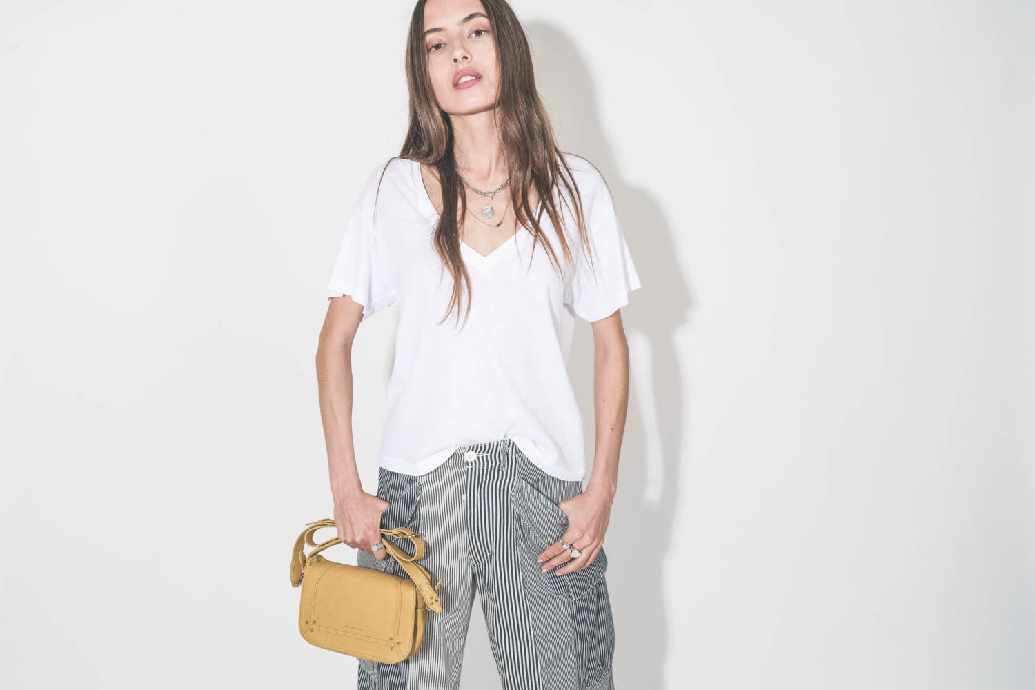 Tee-shirt manches courte col V en coton blanc The Great. Porté avec un pantalon cargo à rayures bleues Railroad R13 et un sac en cuir jaune Mimosa Pepito S Jérôme Dreyfuss. Collier Maria Black et Pascale Monvoisin, bagues en argent Mikuta.