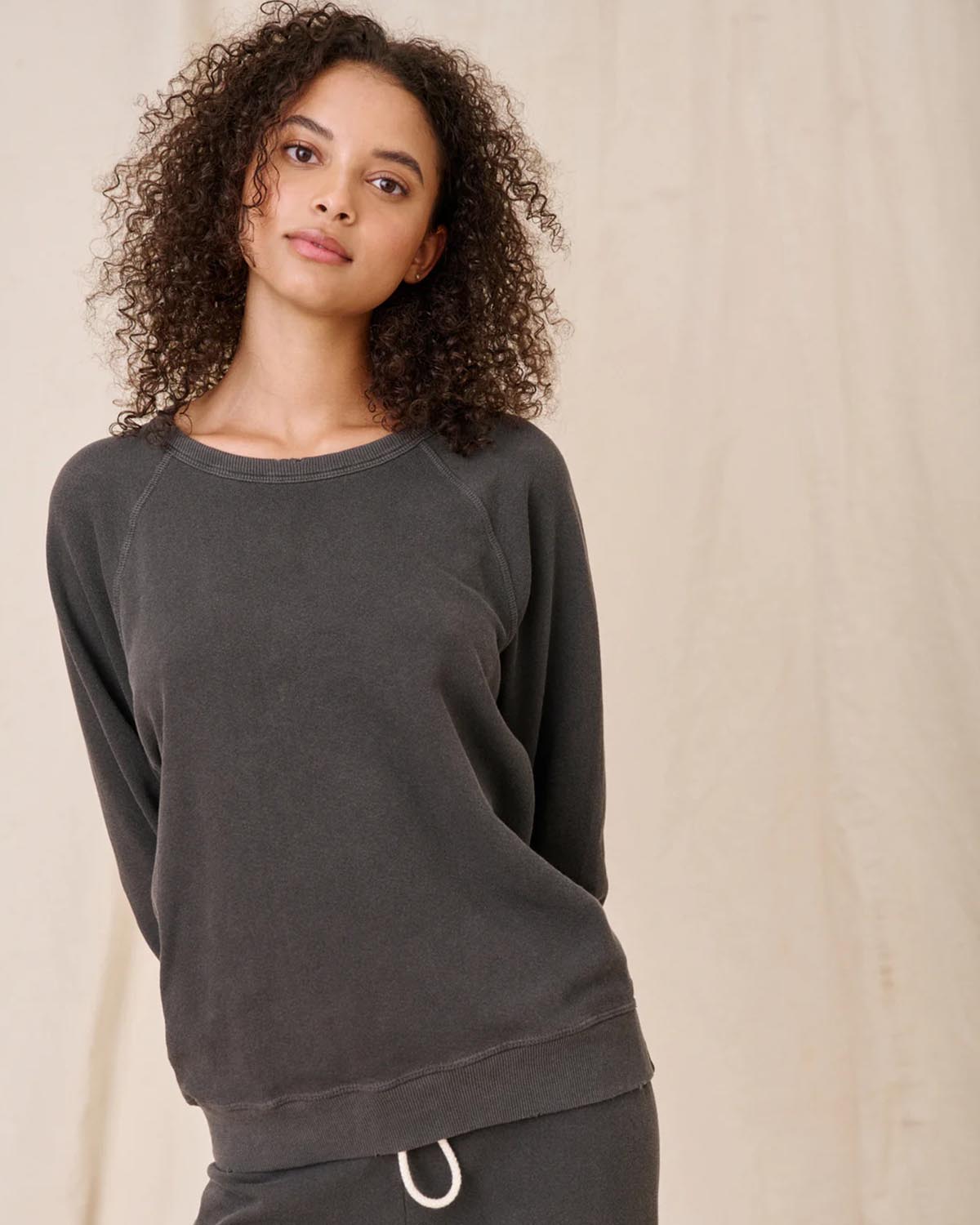 Sweatshirt College en coton noir délavé The Great, porté de face avec un bas de jogging Crop de la même couleur et de la même marque. Détail du sweatshirt effet usé.