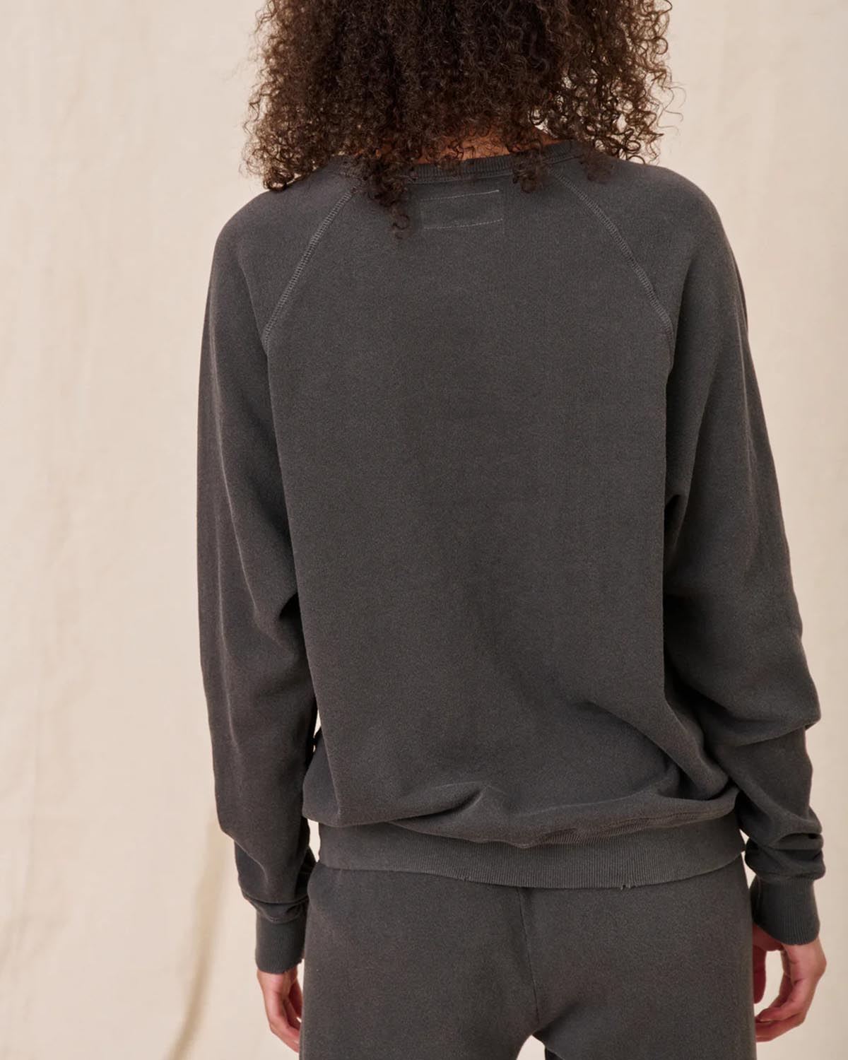 Sweatshirt College en coton noir délavé The Great, porté de dos avec un bas de jogging Crop de la même couleur et de la même marque. Surpiques ton sur ton.