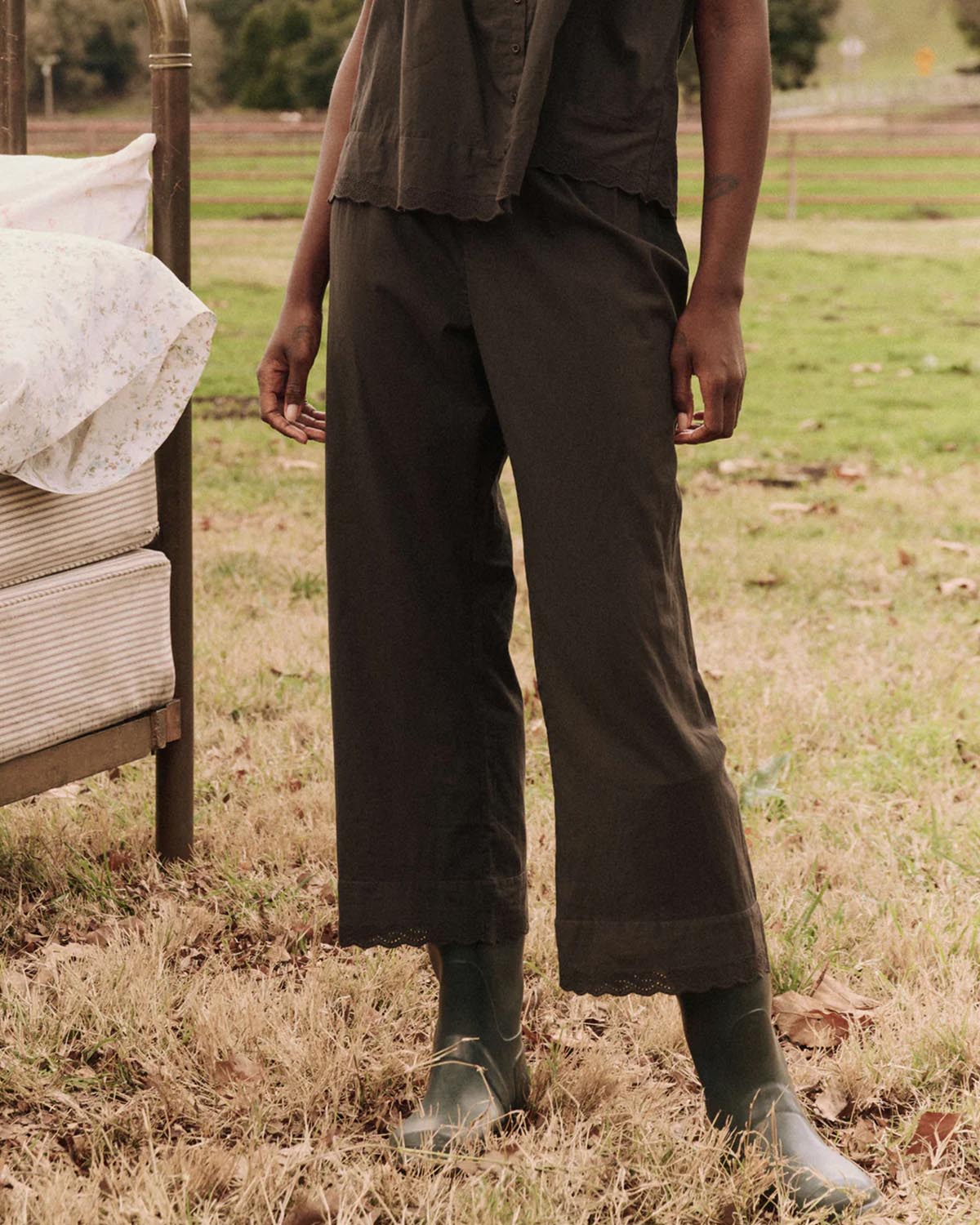 Pantalon taille élastique en coton brodé en bas noir The Eyelet The Great. Thème Sleep. Porté de face avec des bottes.