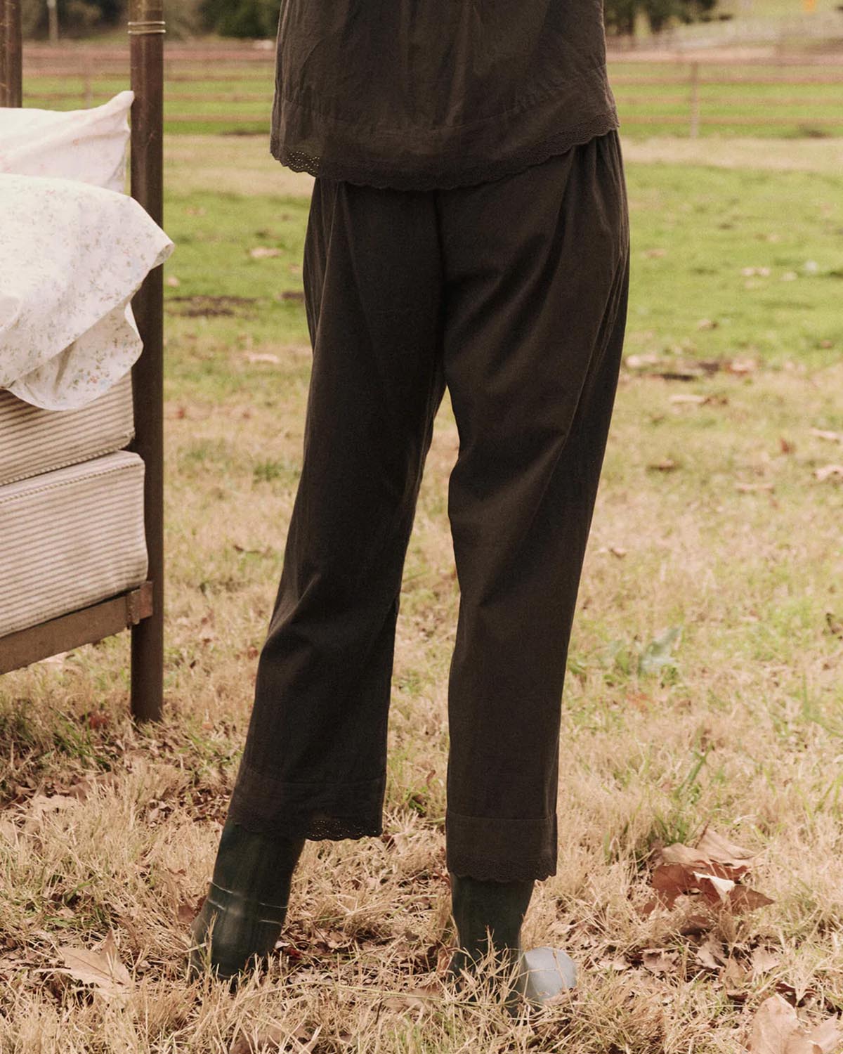 Pantalon taille élastique en coton brodé en bas noir The Eyelet The Great. Thème Sleep. Porté de dos avec des bottes.