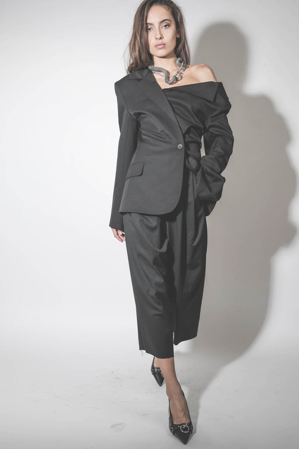 Blazer asymétrique en laine froide noire Anissa Vautrait. Porté avec des escarpins à talons.